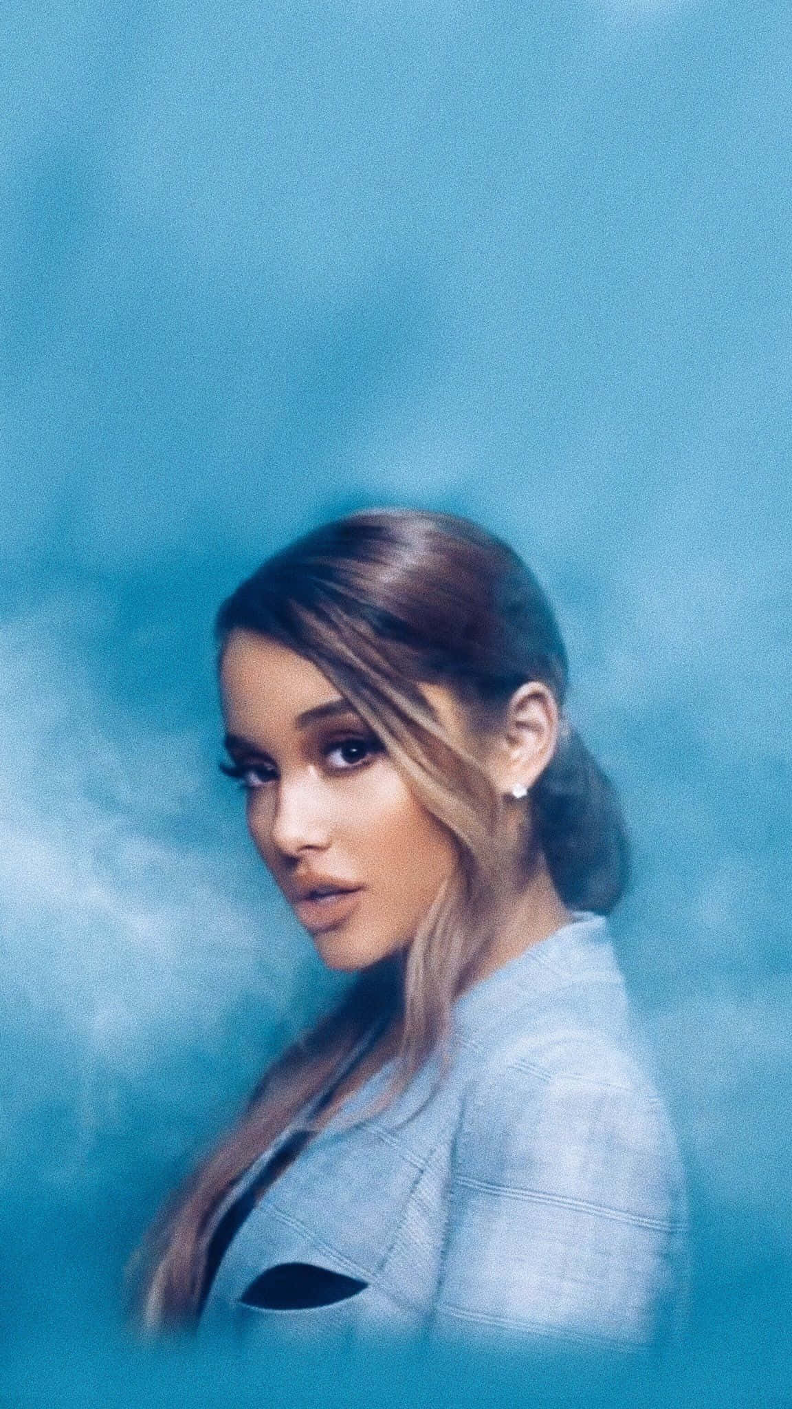 Ariana Grande Aesthetic 桌布 壁紙 — Ariana Grande 在煙霧瀰漫的藍色背景前溫柔凝視，帶有煙霧質感和柔和燈光。