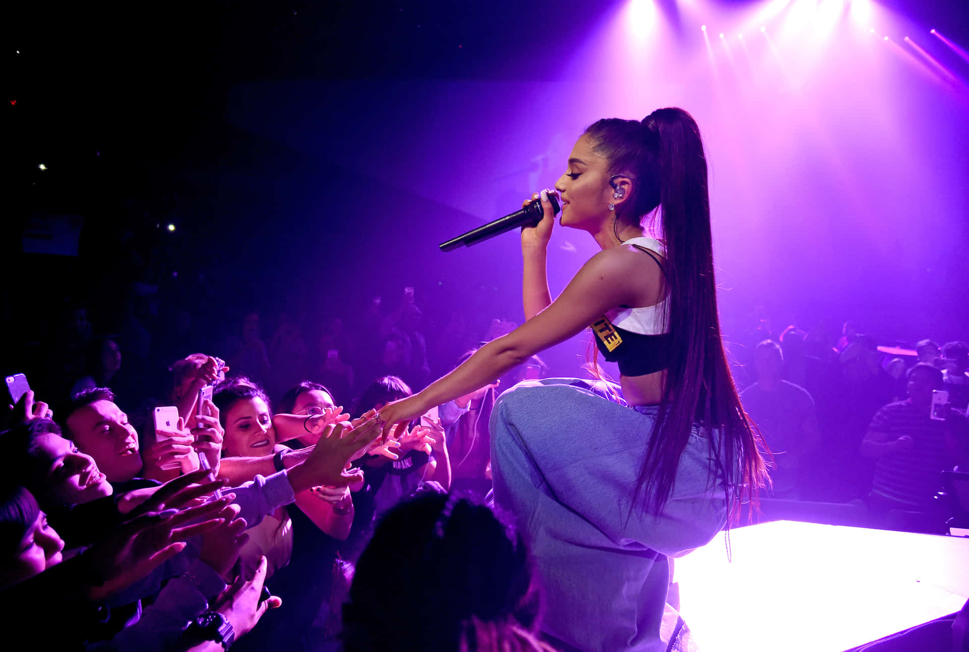 亞莉安娜·格蘭德 桌布 壁紙 — Ariana Grande 在紫色燈光下於舞台上表演，粉絲伸手觸摸她。