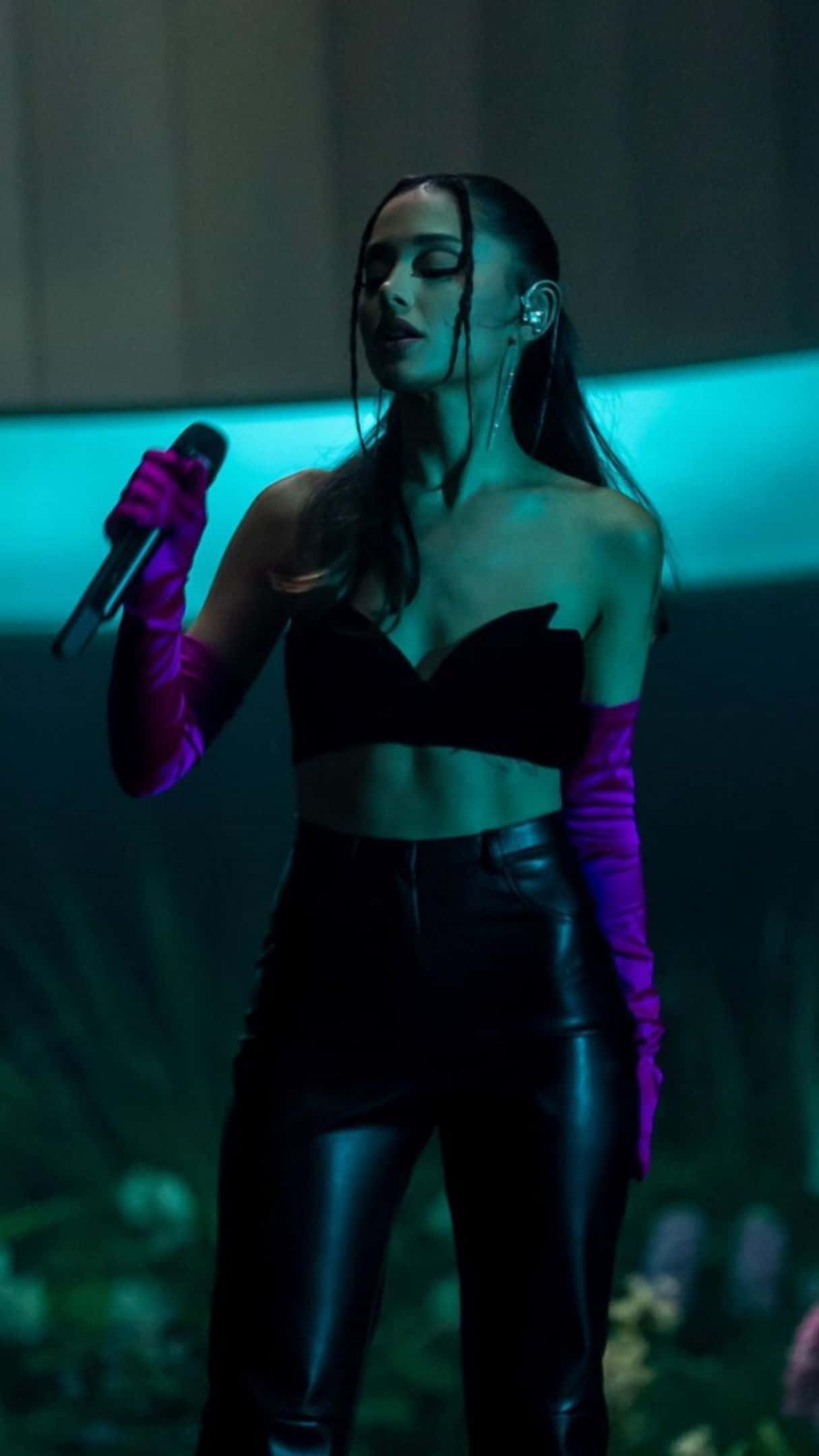 1215x2160 桌布 壁紙 — Ariana Grande 在藍色舞台燈光下穿著黑色服裝和紫色手套在舞台上表演。