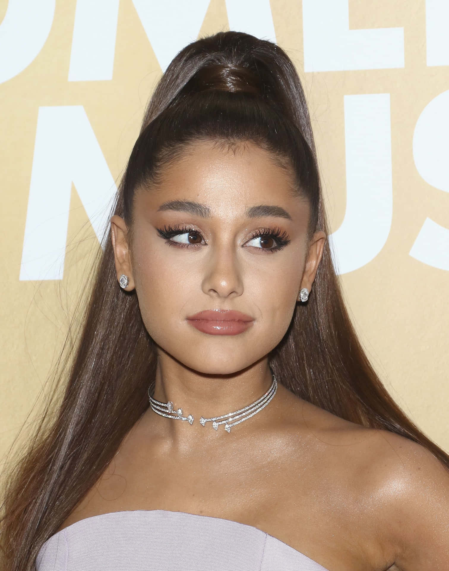 亞莉安娜·格蘭德 桌布 壁紙 — Ariana Grande 在金色背景下，身穿無肩帶薰衣草色長裙，梳著高馬尾，戴著鑽石頸鏈，優雅地擺姿勢。