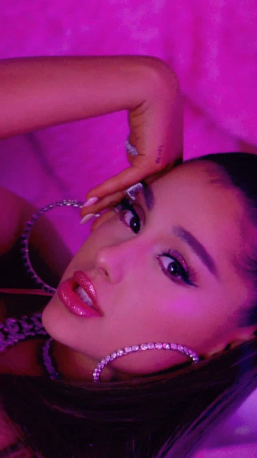 Ariana Grande 7 Rings 桌布 壁紙 — Ariana Grande 在霓虹燈光下，以充滿活力的粉紅色紋理背景襯托，佩戴閃閃發光的鑽石耳環擺姿勢。