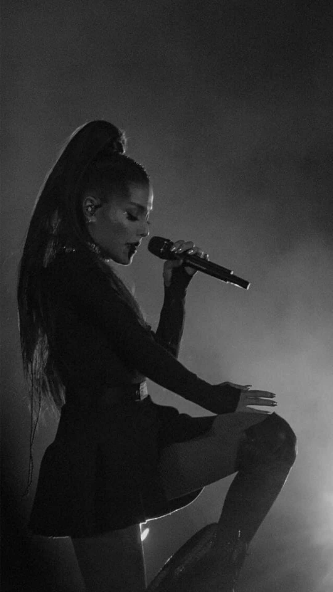 亞莉安娜·格蘭德 桌布 壁紙 — Ariana Grande 在黑白戲劇性燈光和煙霧繚繞的舞台上表演。