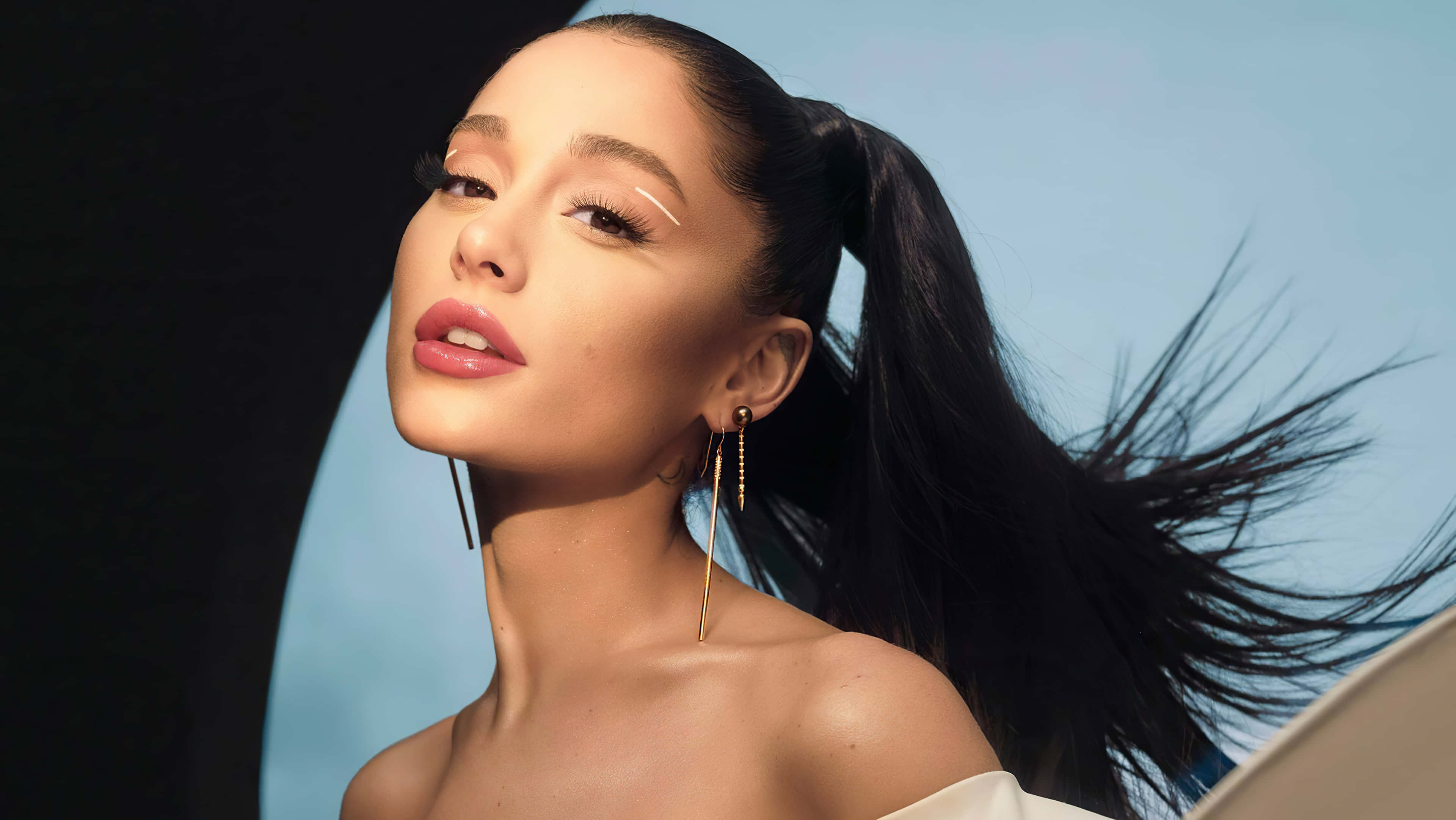 Alluring 桌布 壁紙 — Ariana Grande 抬頭仰望，頭髮隨風飄揚，背景是明亮的藍天和黑暗的背景。