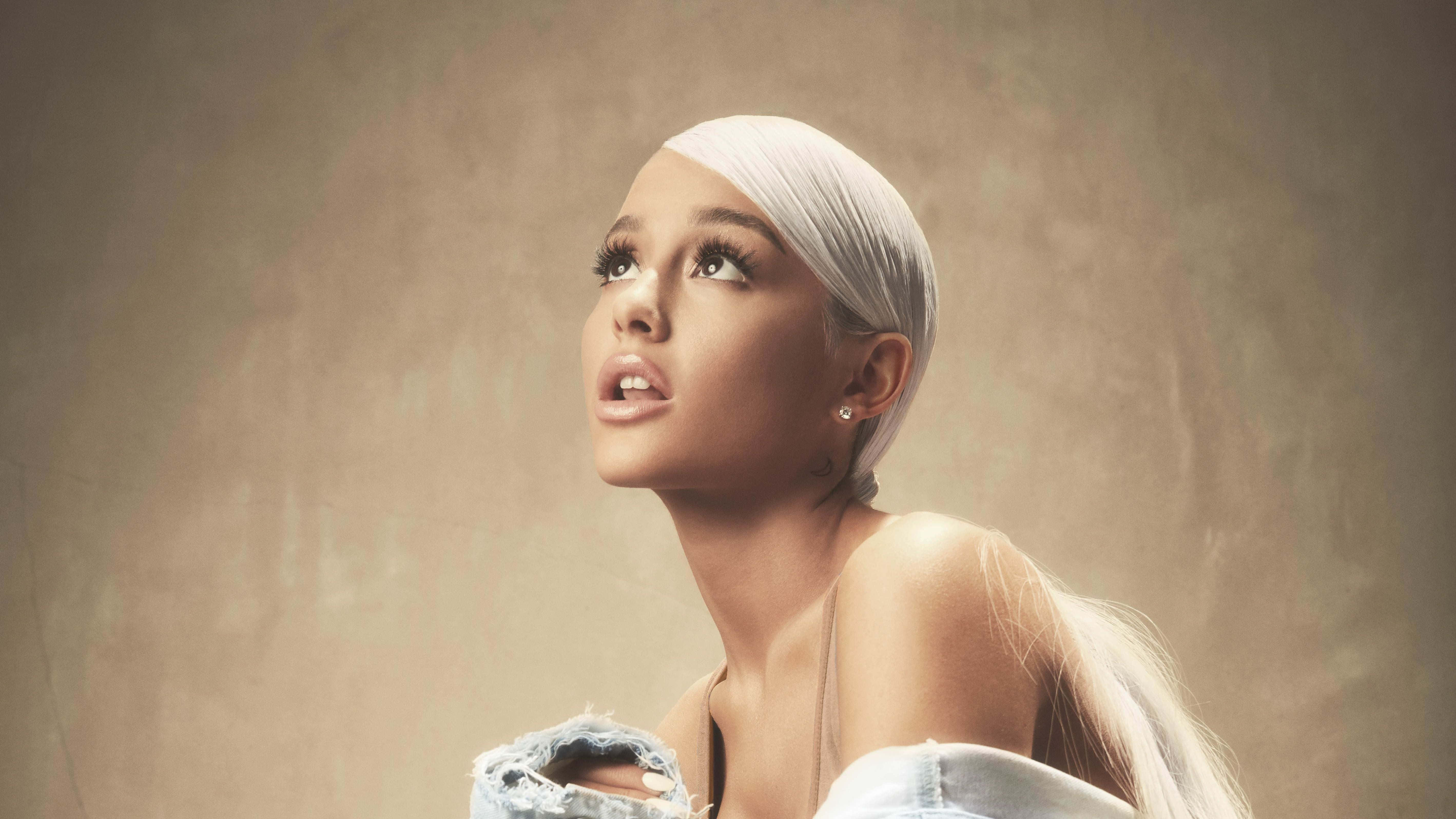 亞莉安娜·格蘭德 桌布 壁紙 — Ariana Grande 擁有鉑金色頭髮，在紋理米色背景下穿著破洞牛仔褲向上凝視。