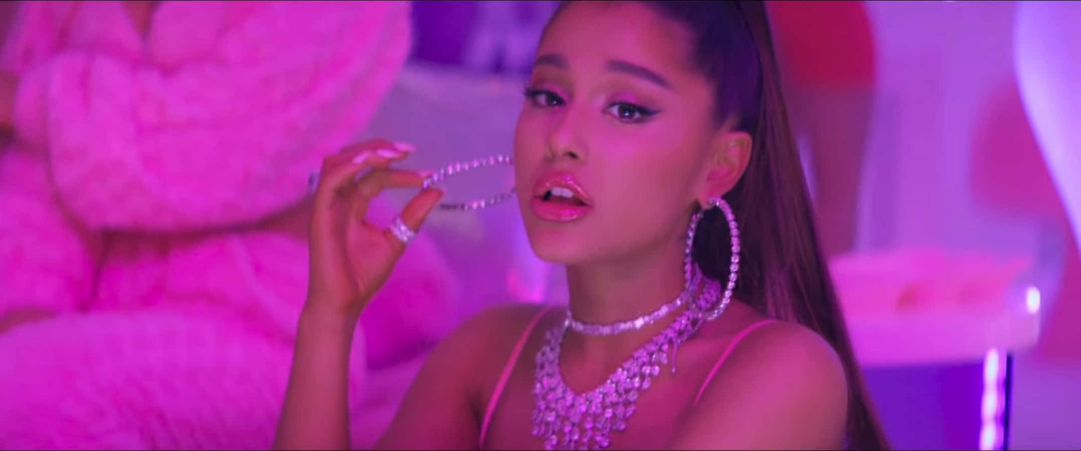 Ariana Grande 7 Rings 桌布 壁紙 — Ariana Grande 穿著閃亮粉紅色服裝，在霓虹粉紅燈光下拿著鑽石項鍊。