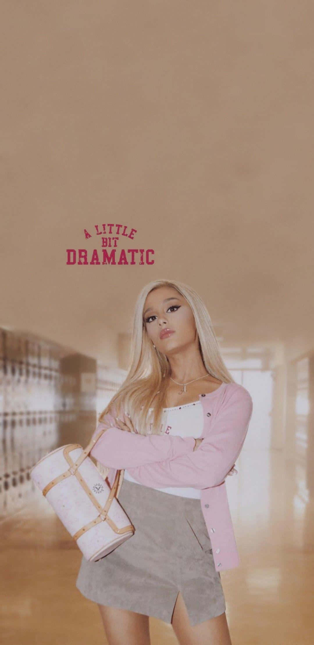 Aesthetic Ariana Grande 桌布 壁紙 — Ariana Grande 自信地站在學校走廊，身穿粉紅色和米色服裝，手持一個白色包包，上方有文字。