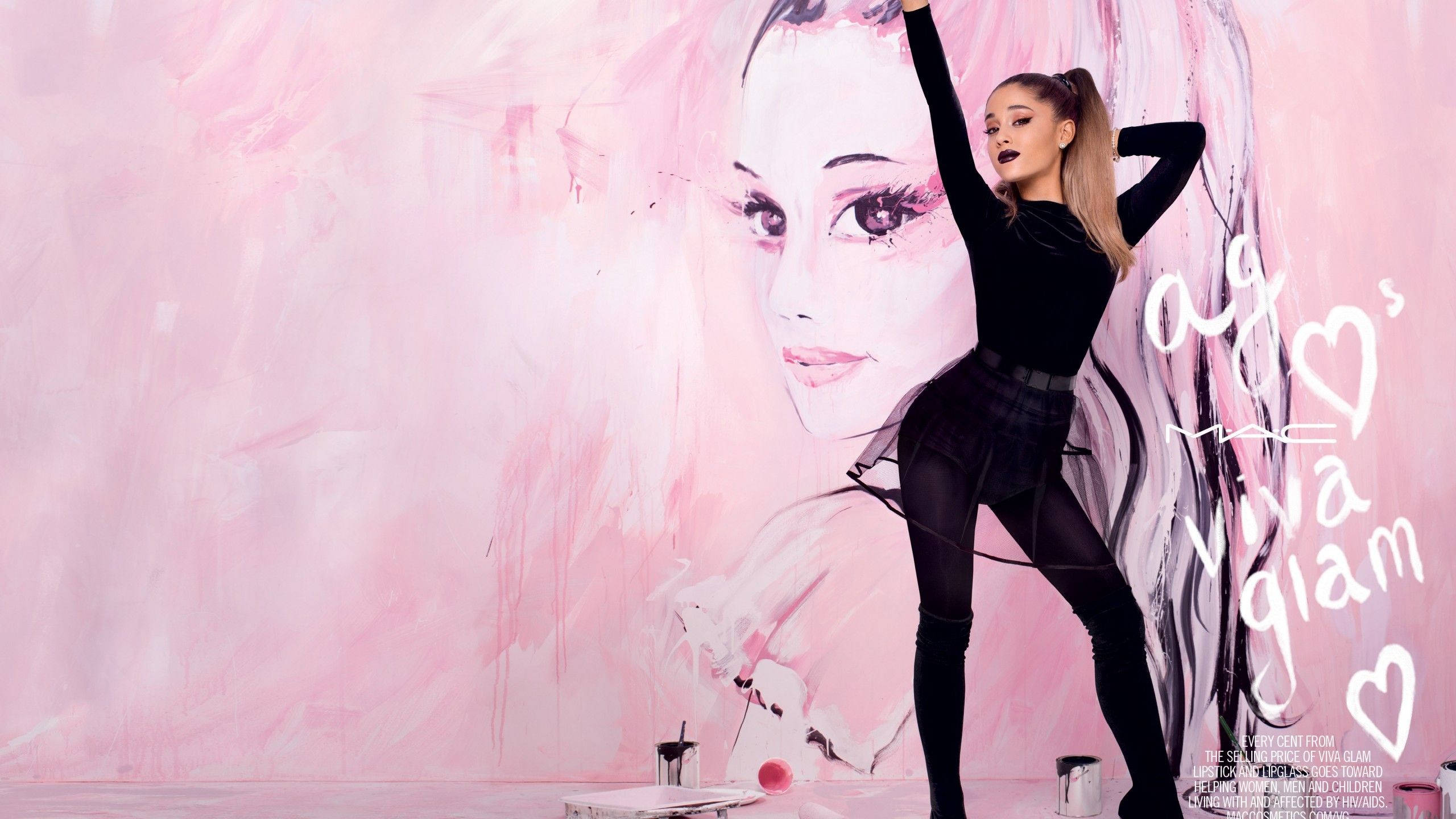 Grande 桌布 壁紙 — Ariana Grande 自信地擺姿勢，面前是一幅大型粉紅色壁畫，畫有她的臉和「Viva Glam」文字。