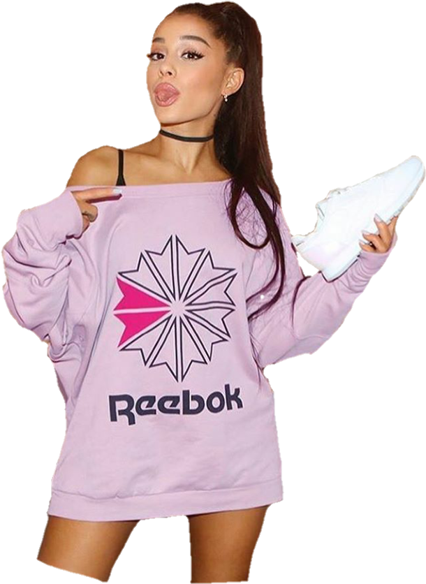 亞莉安娜·格蘭德 桌布 壁紙 — Ariana Grande 身穿淡紫色 Reebok 衛衣，在黑色背景前俏皮地拿著白色運動鞋擺姿勢。
