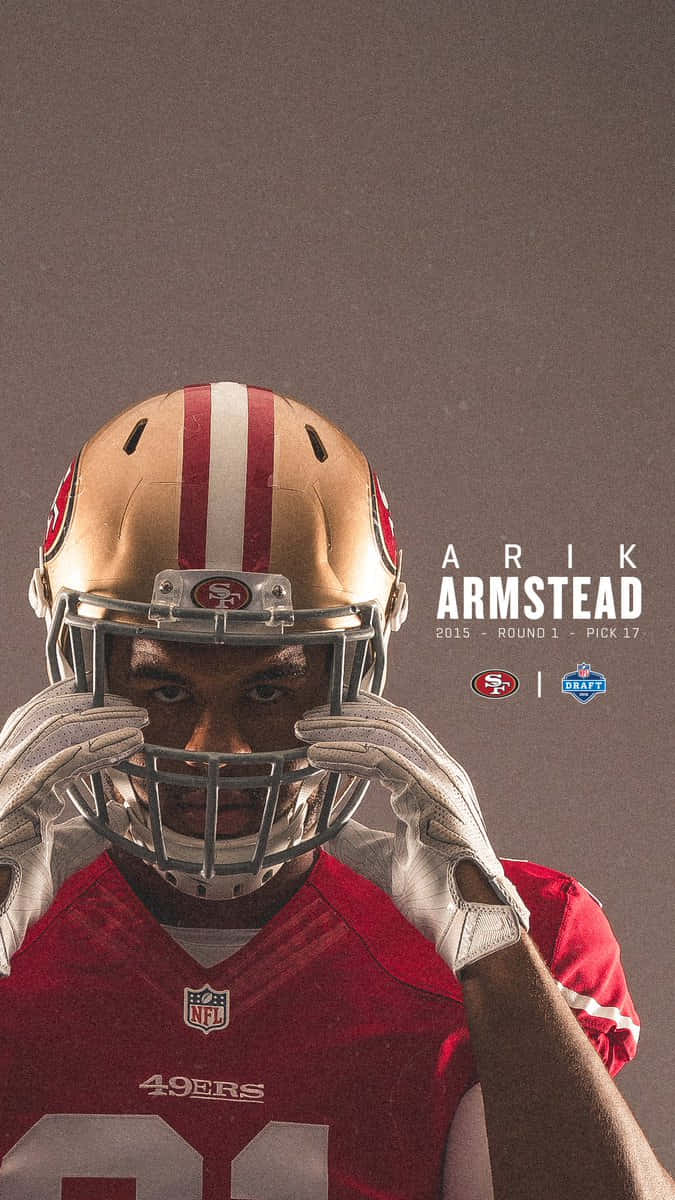 San Francisco 49ers 桌布 壁紙 — Arik Armstead 身穿舊金山49人隊裝備，舉起頭盔，在柔和的灰色背景上露出銳利的眼睛。