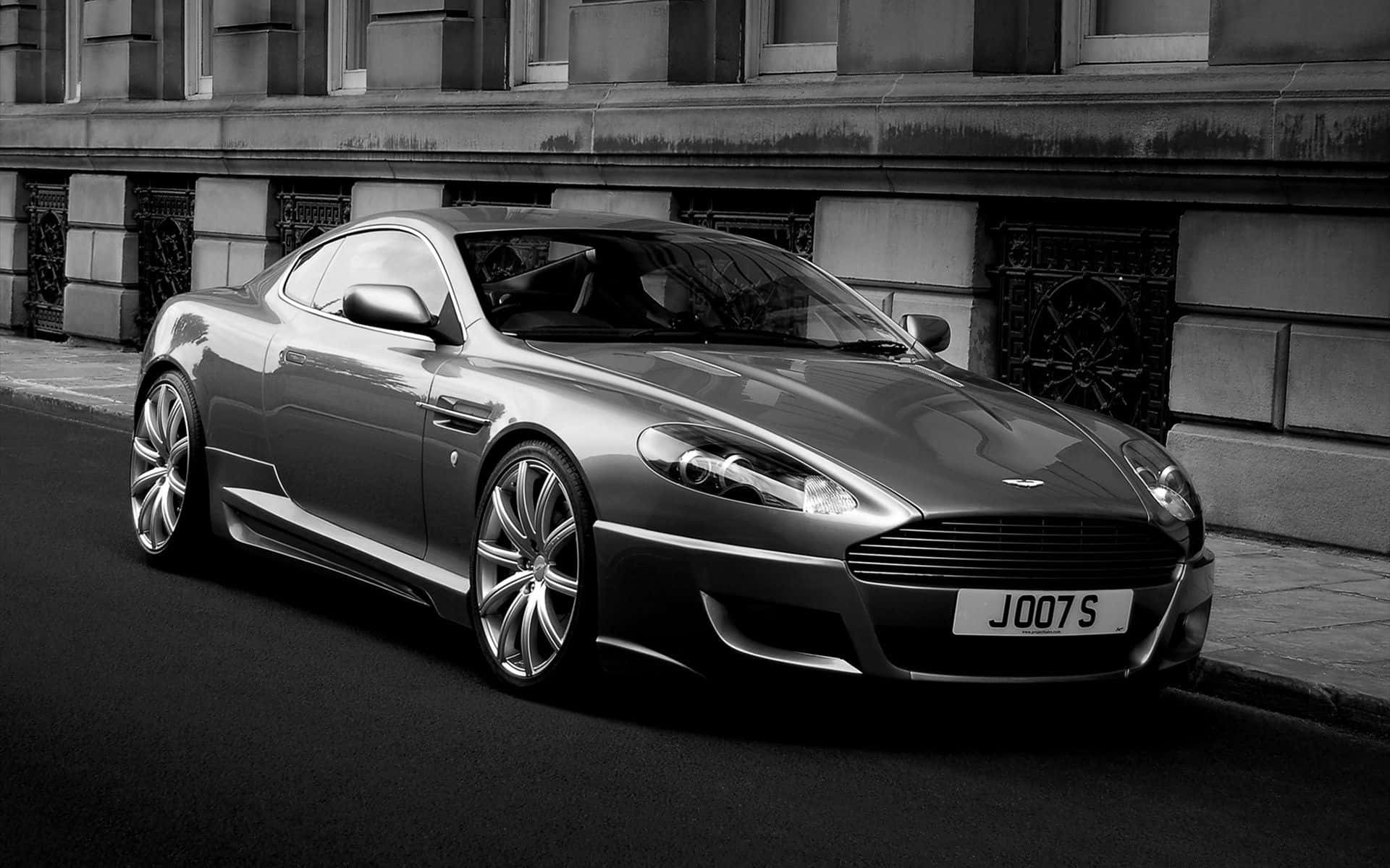 Aston Martin DB9 豪華跑車 壁紙 — 一架時尚的銀色Aston Martin跑車，在單色調的城市街道上，帶有戲劇性的燈光效果。