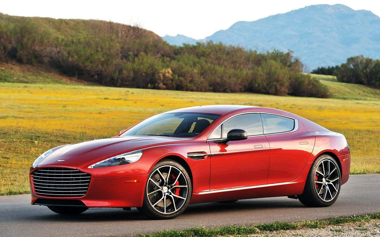 Aston Martin Rapide S：時尚豪華與性能 壁紙 — 一輛流線型紅色Aston Martin跑車沿著蜿蜒的道路行駛，穿過陽光明媚的田野，遠山在望。