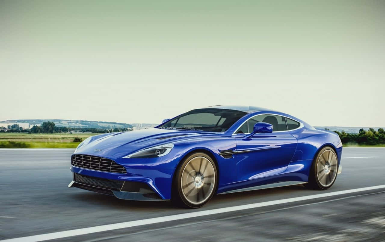 體驗Aston Martin Vanquish的力量與優雅 壁紙 — 一架流線型藍色Aston Martin跑車在柔和陰天下沿鄉村高速公路飛馳。