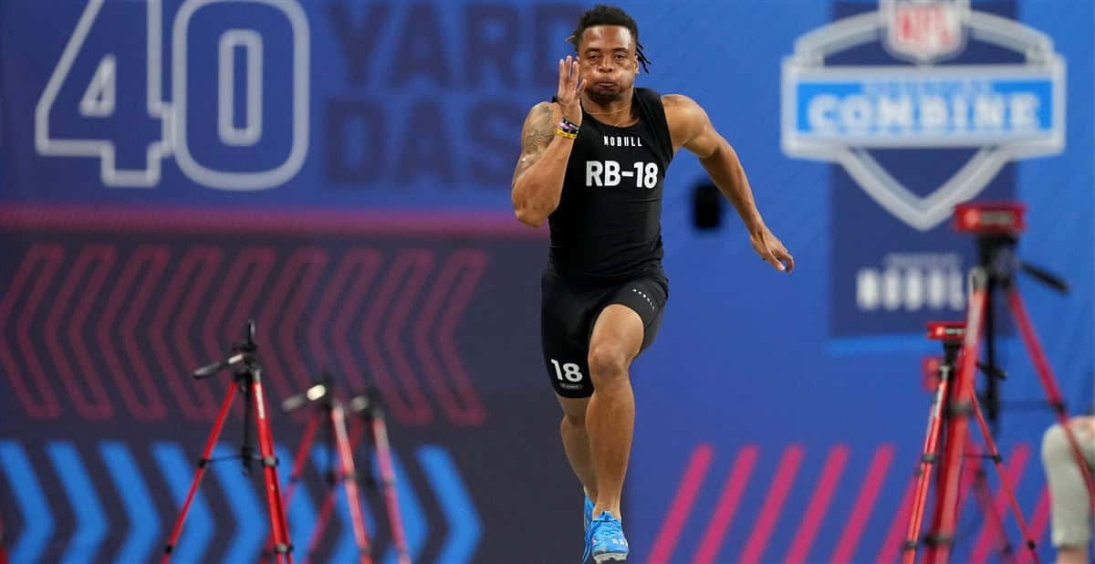  壁紙 — 身穿黑色RB-18球衣的運動員在NFL聯合測試中衝刺經過40碼衝刺標記，攝影機捕捉他的動作。