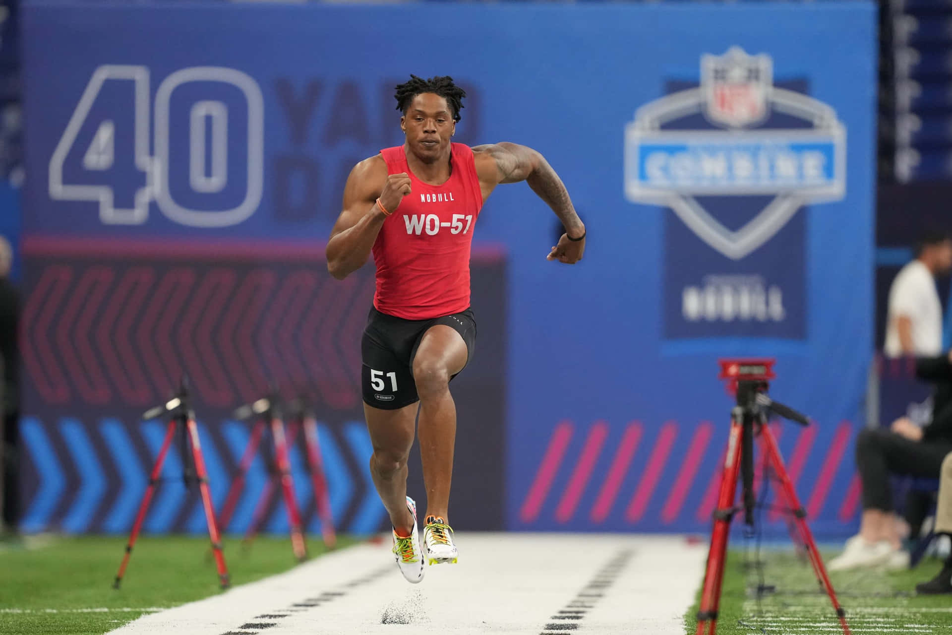  壁紙 — 身穿紅色背心的運動員在NFL聯合測試賽中專注地衝刺40碼短跑賽道。