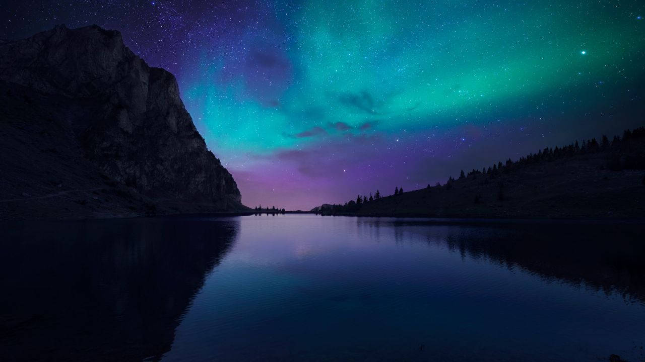 北極光在繁星點點的湖面和山脈剪影上方發光。 — 4K 壁紙