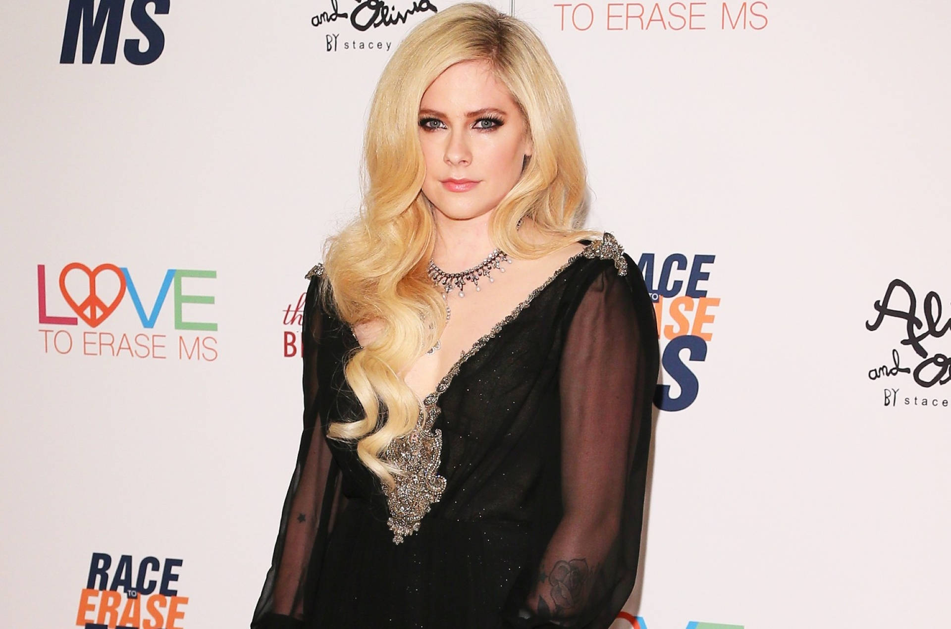 Avril 桌布 壁紙 — Avril Lavigne 在一個有品牌背景的慈善活動中，穿著帶有銀色裝飾的黑色透視長袍擺姿勢。