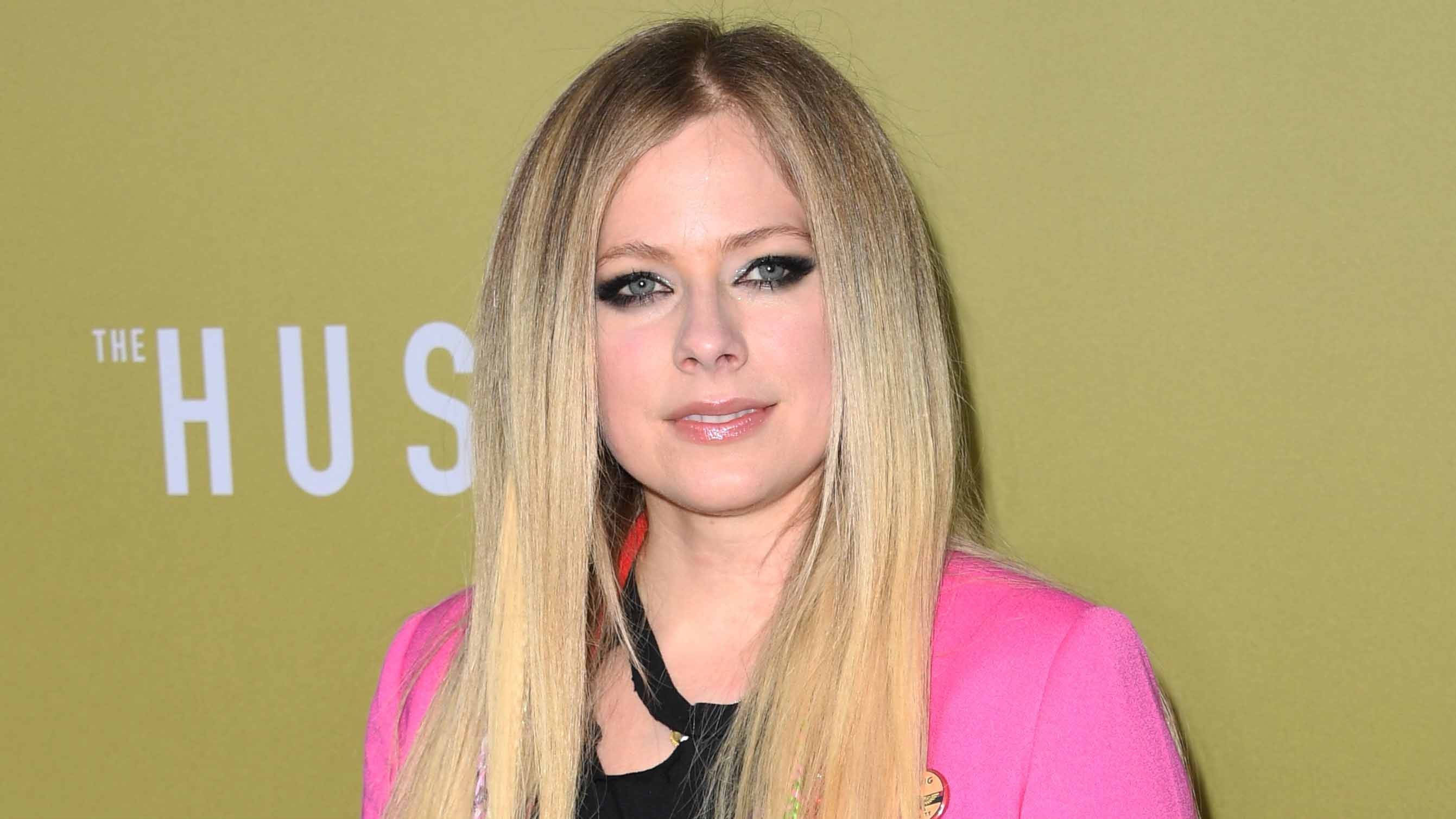 Avril 桌布 壁紙 — Avril Lavigne 穿著亮粉紅色西裝外套，在柔和的綠色背景前擺姿勢，背景有部分白色文字。