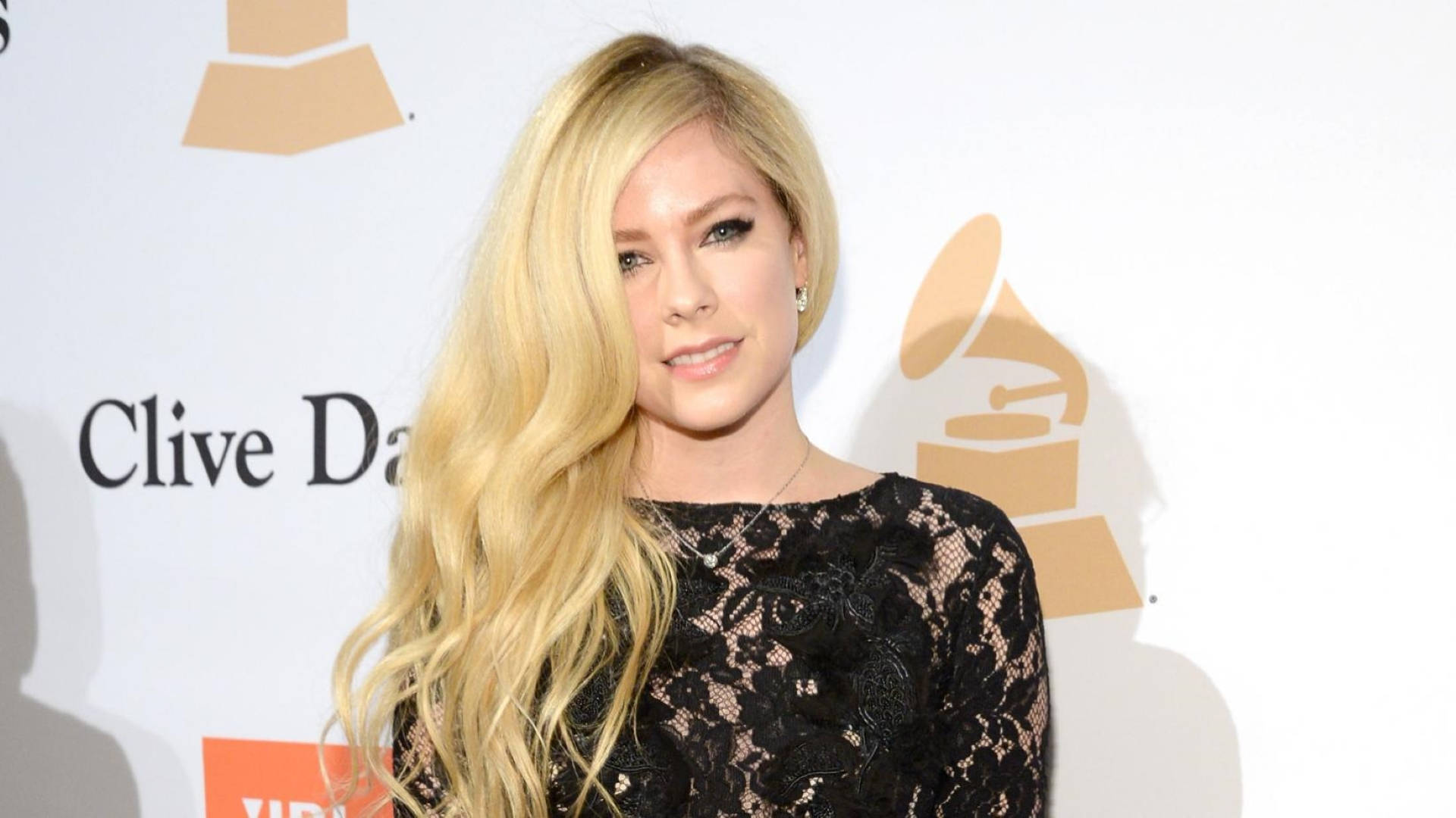 Avril 桌布 壁紙 — Avril Lavigne 穿著黑色蕾絲連衣裙，在帶有金色標誌的白色葛萊美獎背景前擺姿勢。