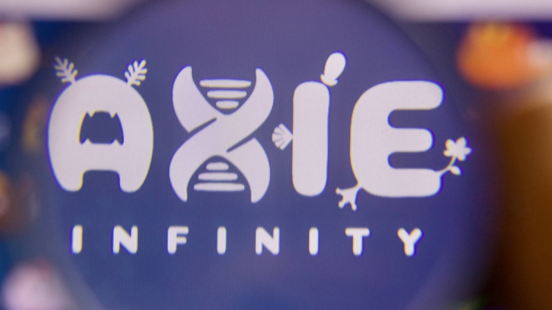 infinity 桌布 壁紙 — Axie Infinity 標誌特寫，在深藍色螢幕上發出白色光芒，周圍有柔和模糊的燈光。
