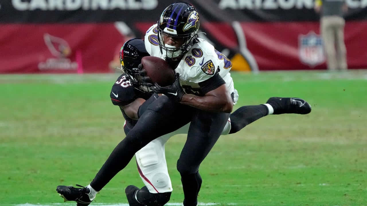  壁紙 — 一名身穿白色和紫色球衣的巴爾的摩烏鴉隊球員在NFL比賽中於綠色球場上被一名身穿黑色球衣的亞特蘭大獵鷹隊球員擒抱。