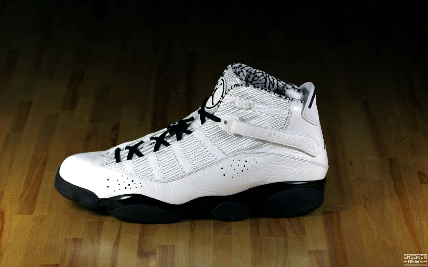 白色 Air Jordan 12 運動鞋，帶有黑色細節，置於木地板上。 — Jordan Logo 壁紙