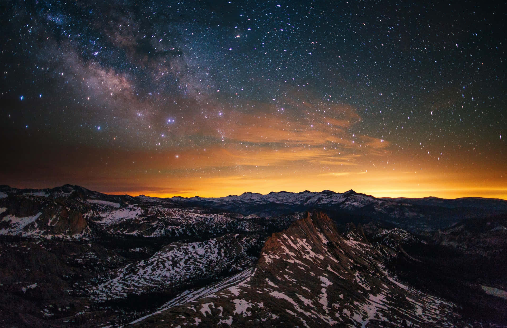在星空夜晚下，白雪覆蓋的山脈，地平線閃耀橙色光芒。 — Macbook Pro 壁紙