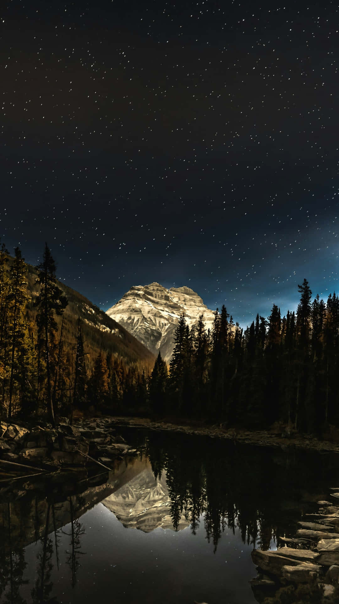  壁紙 — 白雪覆蓋的山峰在星空下完美地倒映在由深色松樹環繞的平靜湖面上。