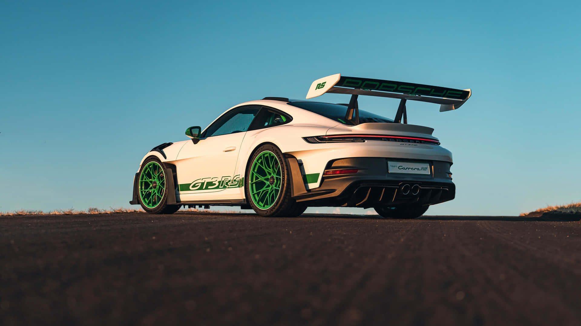  壁紙 — 一輛白色保時捷911 GT3 RS，帶有綠色點綴和大型尾翼，停在晴朗藍天下的賽道上。