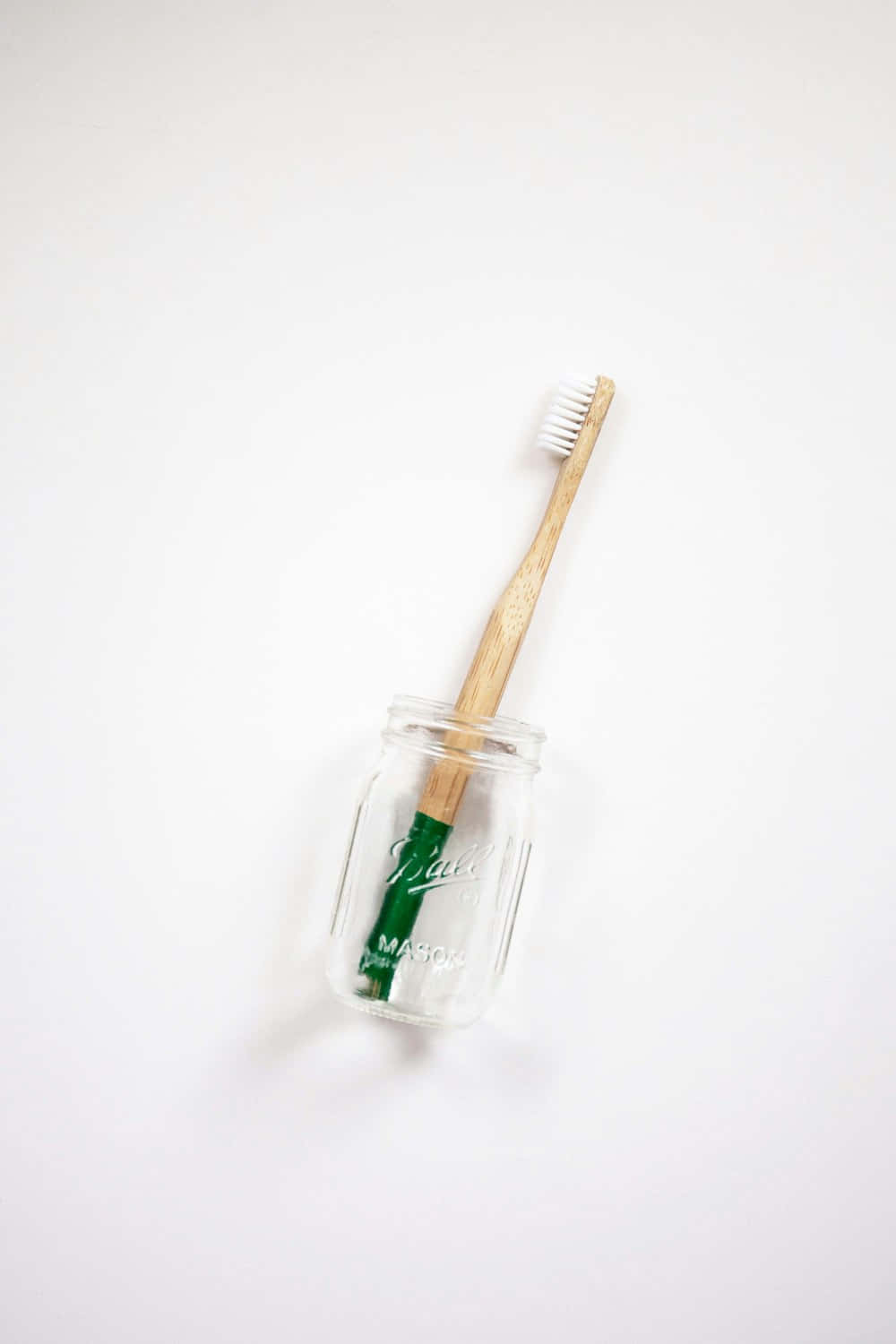  壁紙 — 一把綠色手柄的竹牙刷直立放在透明玻璃梅森罐中，背景為純白色。