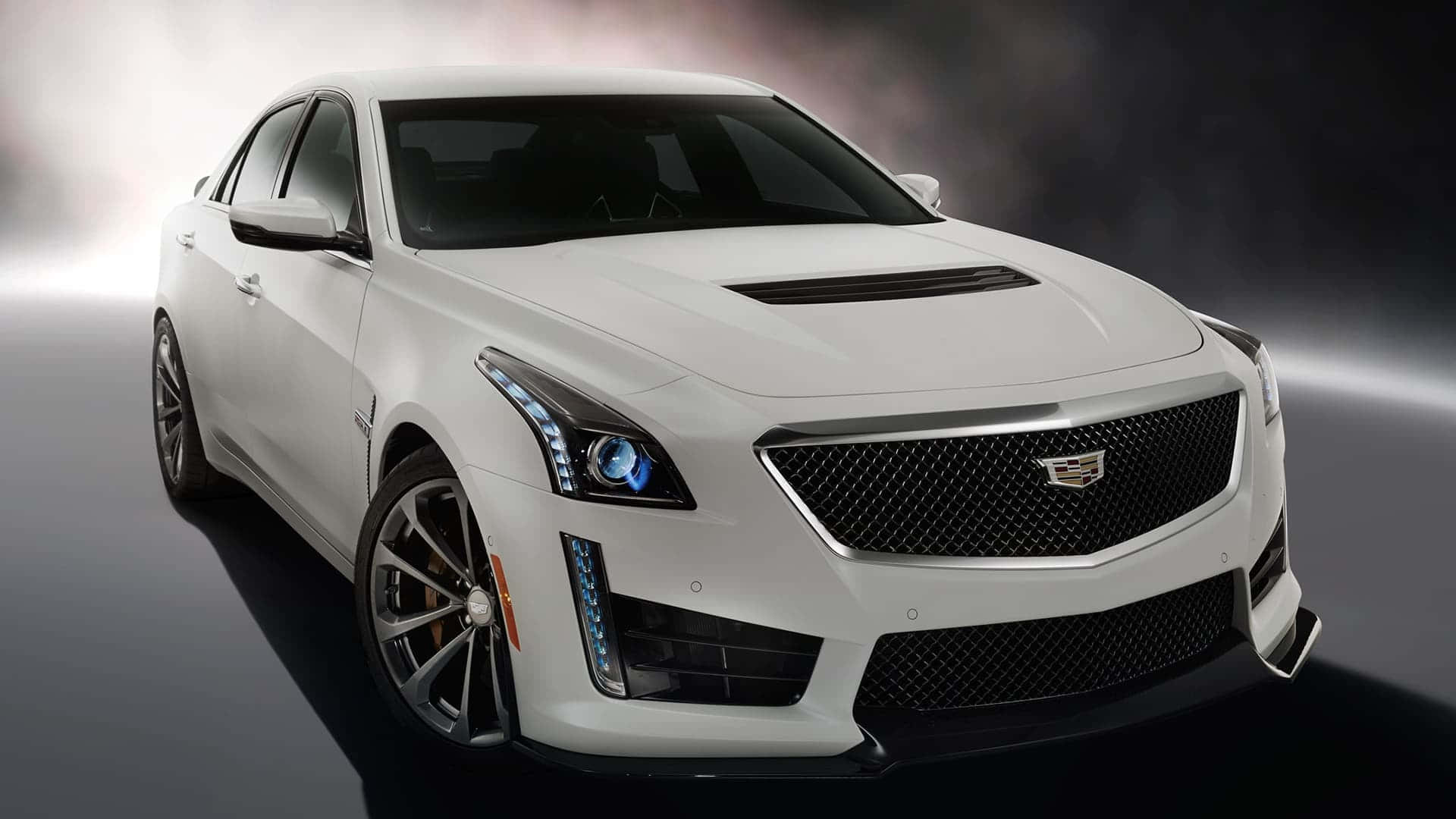 Cadillac Cts 桌布 壁紙 — 一輛時尚的白色Cadillac CTS-V運動轎車在戲劇性的攝影棚燈光下閃耀，煙霧在其激進的前格柵和鋒利頭燈周圍旋轉。