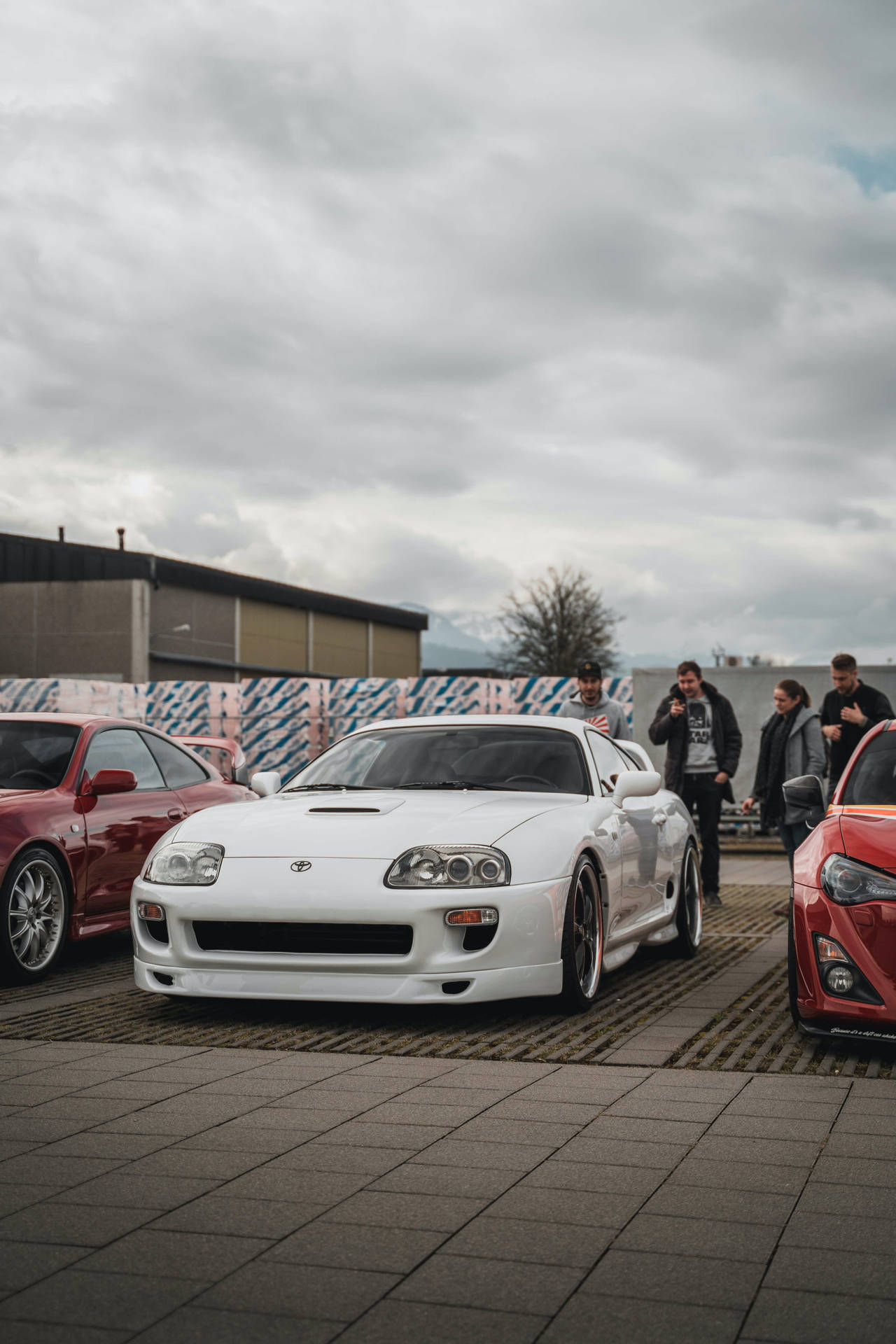 一群人在陰天戶外車展上欣賞白色跑車。 — Toyota Supra 壁紙