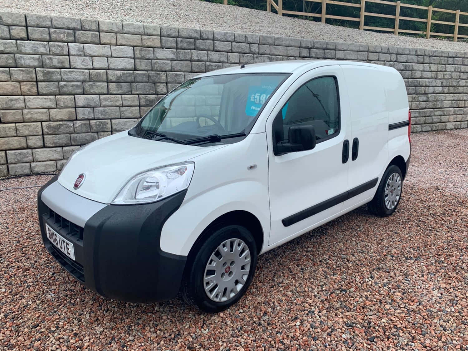 Fiat Fiorino 桌布 壁紙 — 一輛白色 Fiat Fiorino 廂型車停放在碎石上，背景有石牆和木柵欄。