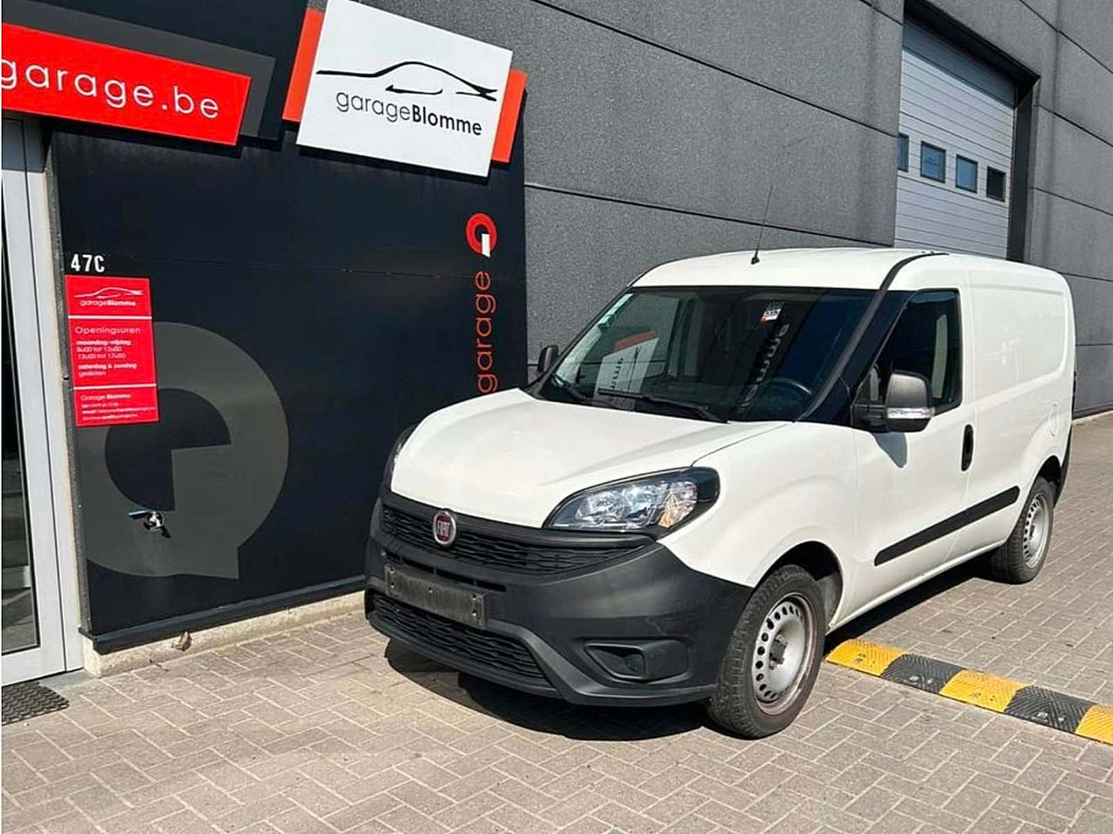  壁紙 — 一輛白色Fiat Fiorino廂型車停放在現代化車庫外的鋪砌場地上，車庫帶有醒目的招牌。