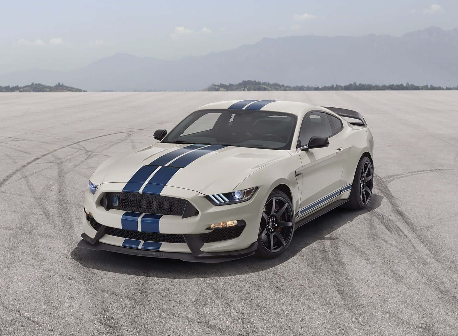 Ford Mustang Shelby Gt350 桌布 壁紙 — 一台帶有藍色賽車條紋的白色福特野馬，停放在廣闊的沙漠跑道上，遠山在朦朧的天空下若隱若現。