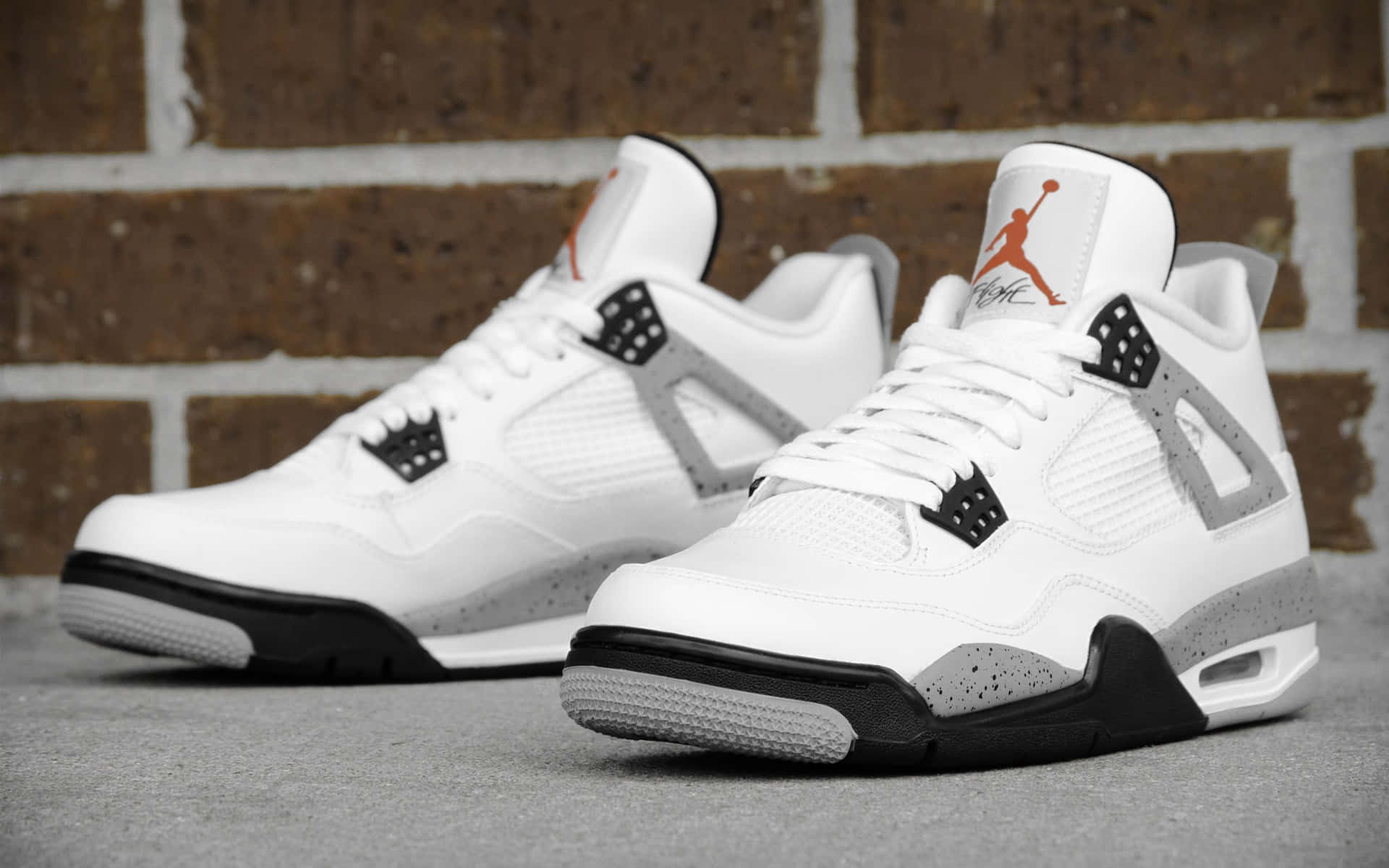 白色Jordan 4運動鞋，黑色和橙色細節，背景為磚牆。 — Air Jordan 壁紙