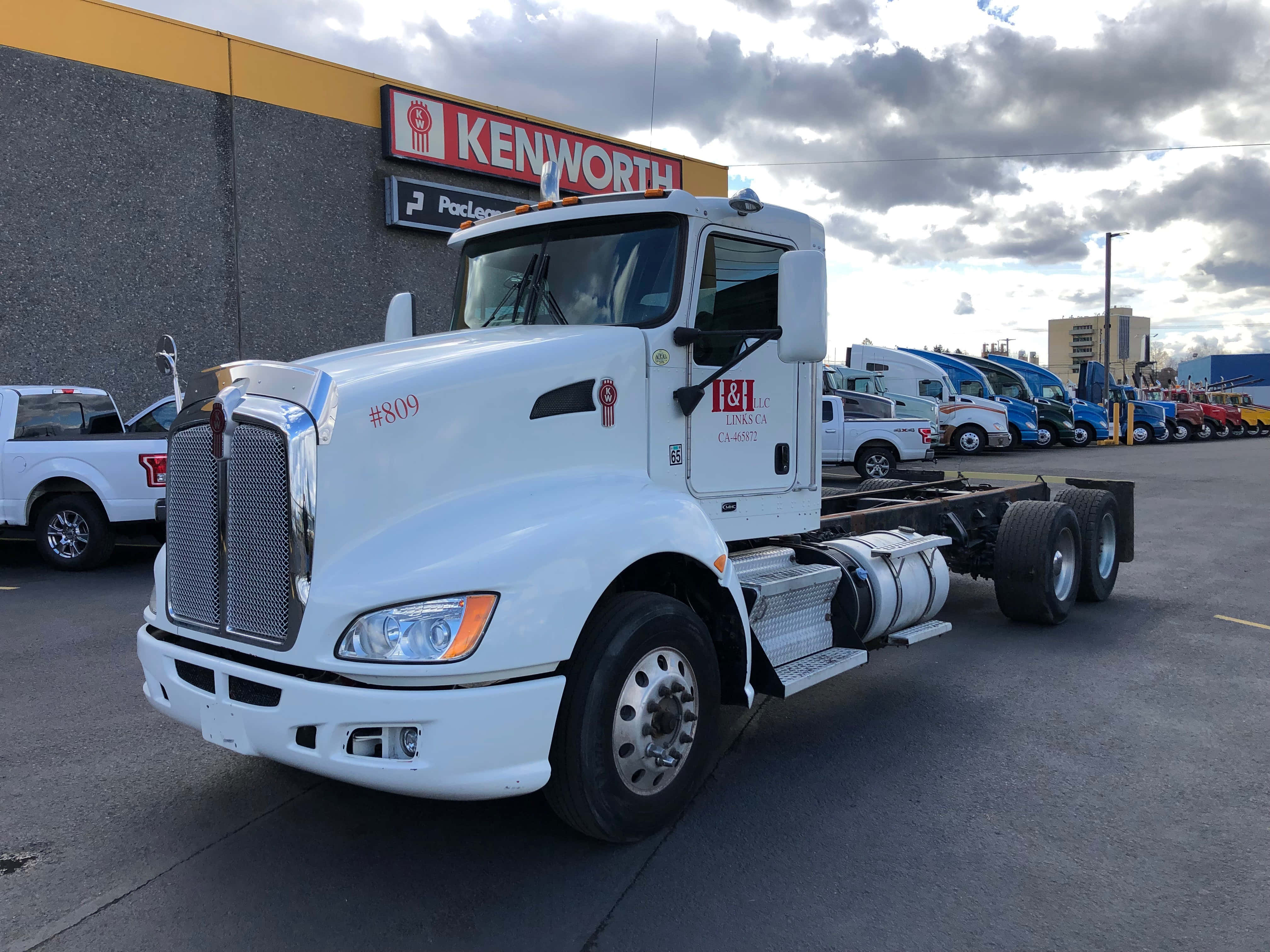 Kenworth T660 桌布 壁紙 — 一輛純白色Kenworth半拖車車頭停放在經銷商場地，天空多雲，後面有其他卡車排成一列。