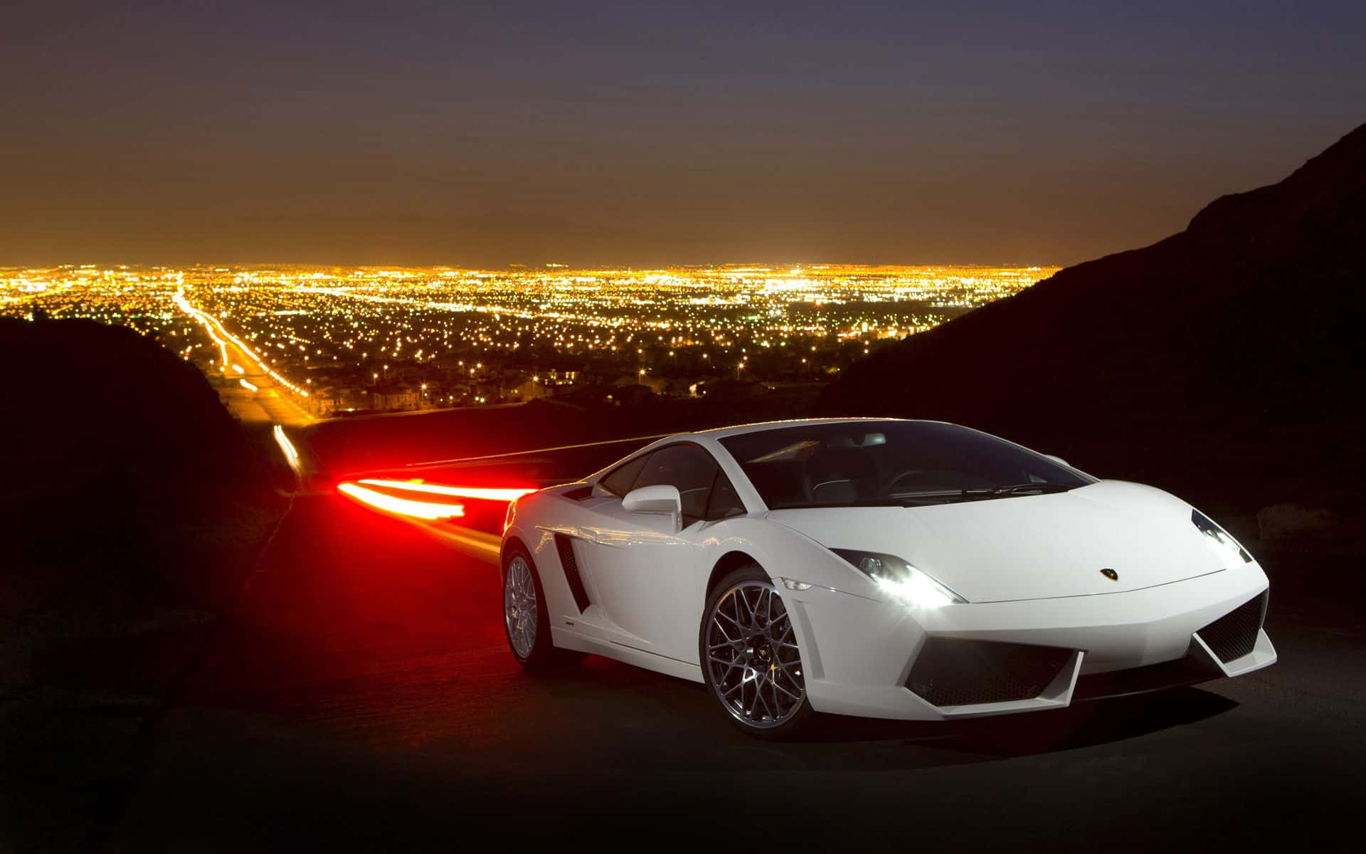 Lamborghini Gallardo 桌布 壁紙 — 一輛白色藍寶堅尼跑車在夜間滑行，紅色尾燈閃爍，背景是廣闊的金色燈光城市景觀。