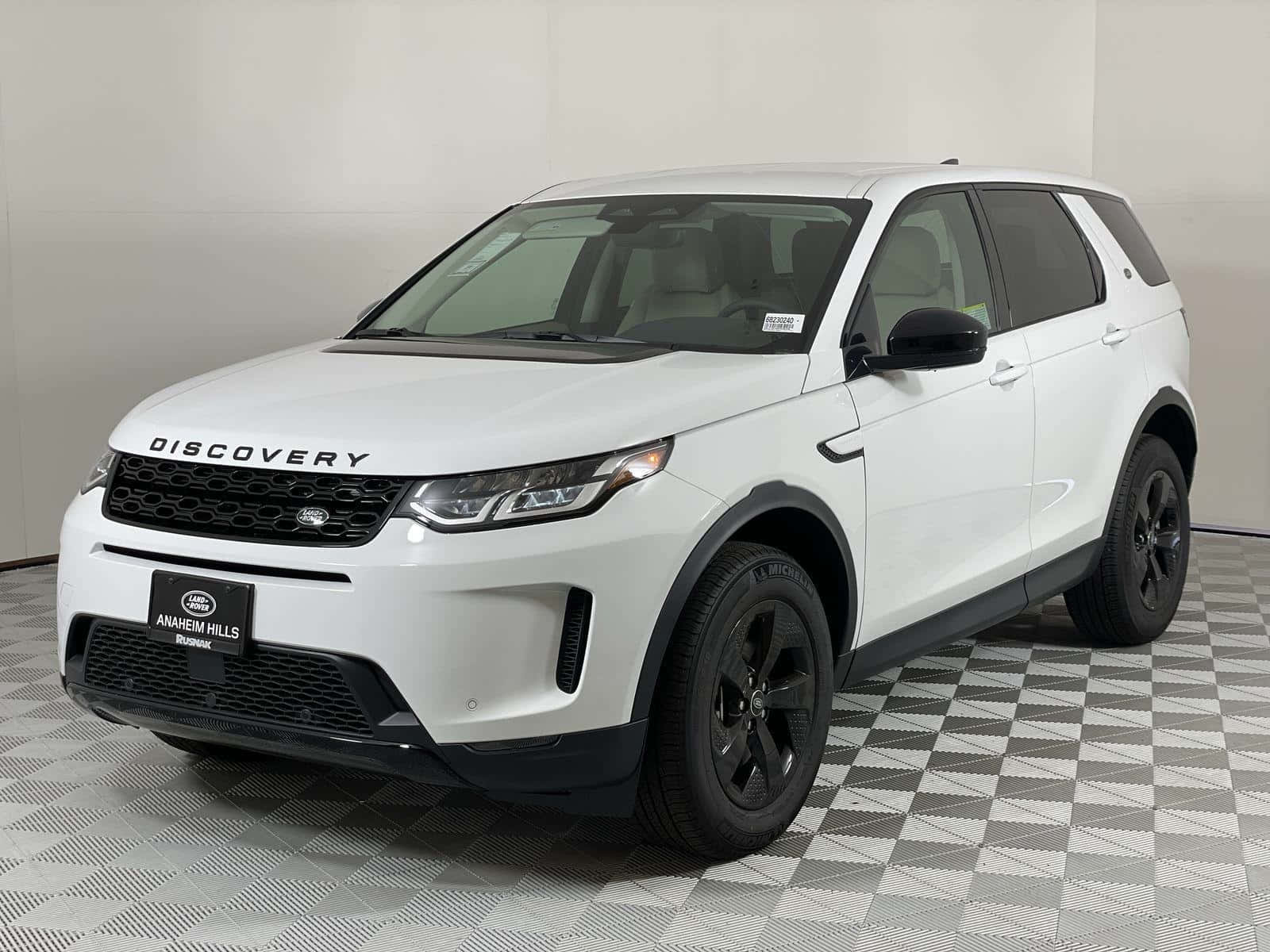 Land Rover Discovery 桌布 壁紙 — 一輛純白色的 Land Rover Discovery SUV 帶有黑色飾件，站在明亮室內展廳的棋盤格地板上。