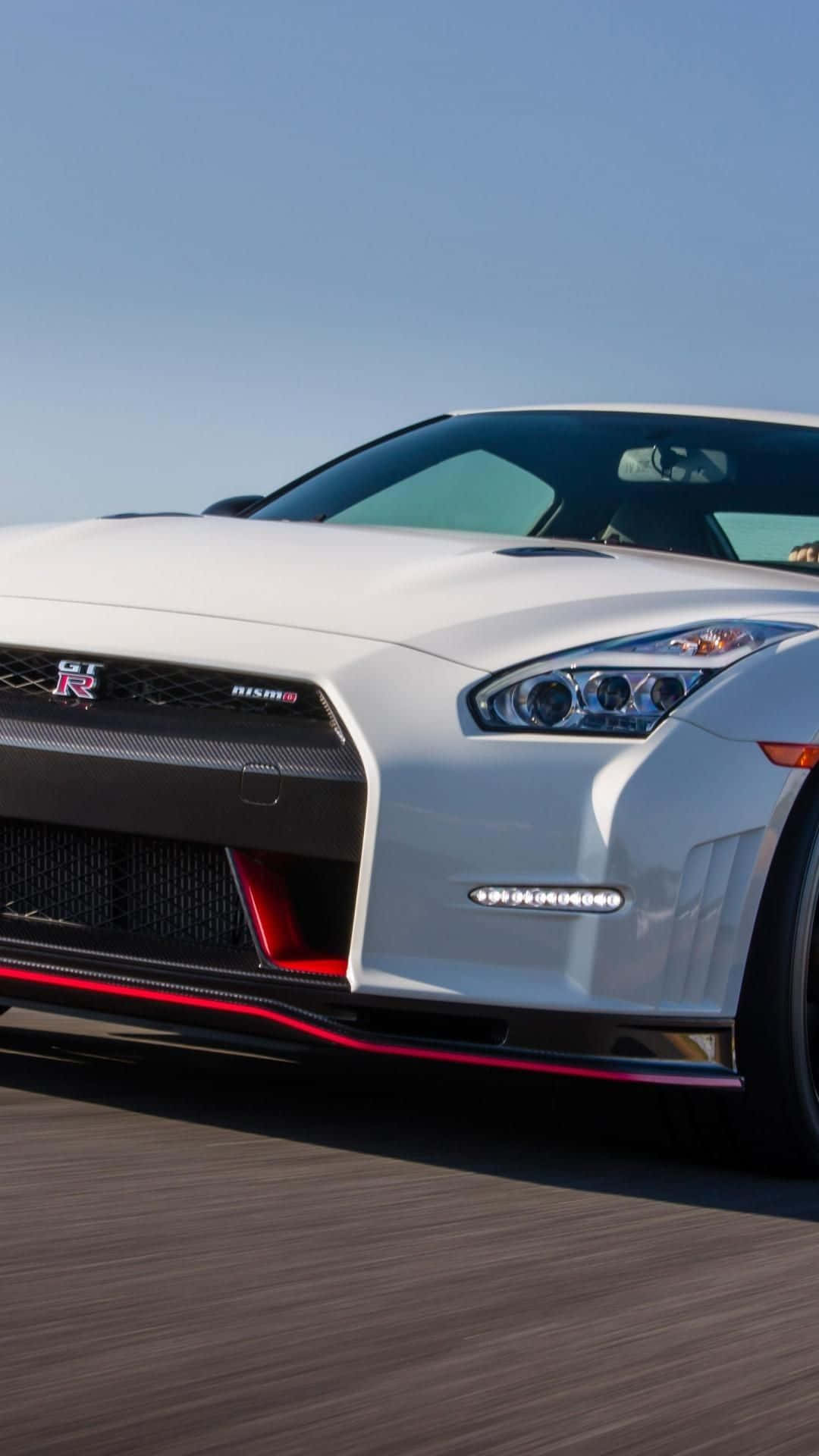 白色日產GT-R Nismo跑車在道路上飛馳，帶有紅色點綴。 — 吉他 iPhone 壁紙