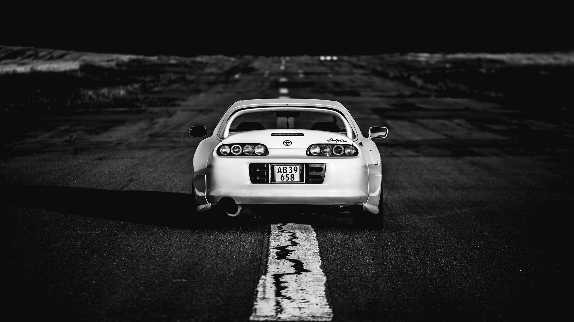 白色跑車在夜晚停放在裂開的道路上，背景是黑暗的地平線。 — Toyota Supra 壁紙
