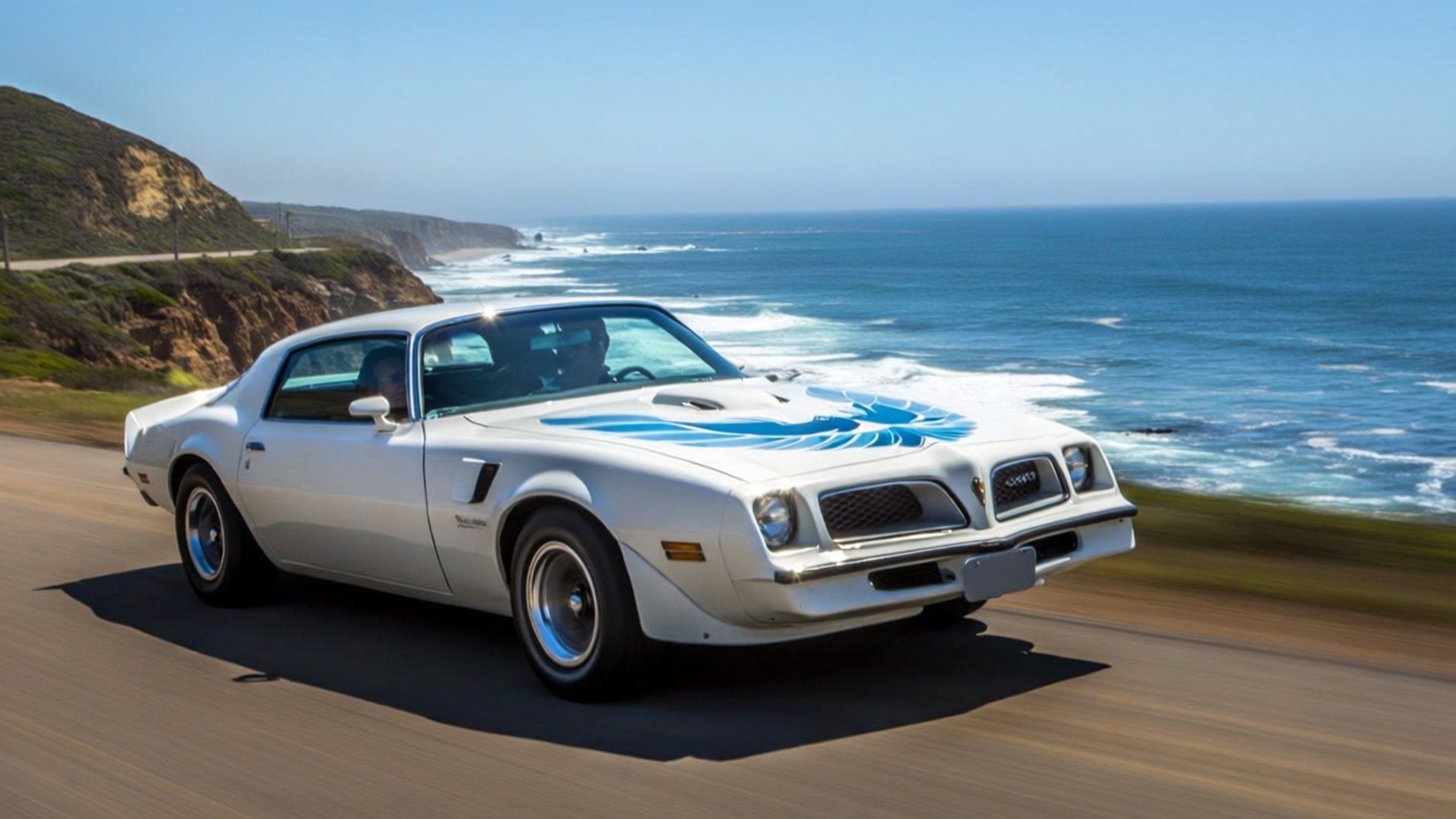 Coastal Trans Am Cruise 壁紙 — 一輛帶有藍色火焰貼花的白色1970年代龐蒂亞克火鳥，沿著海岸高速公路奔馳，旁邊是拍打的海浪，天空清澈湛藍。