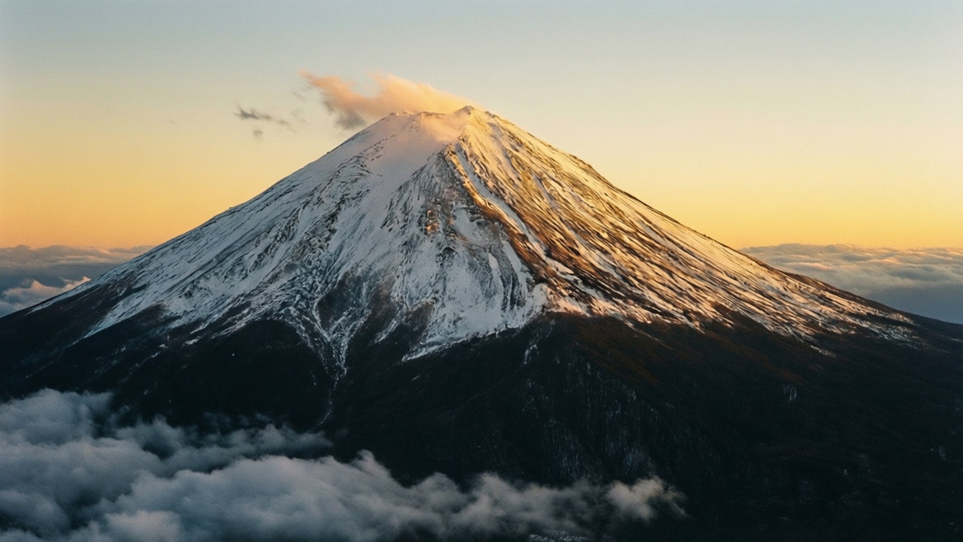Snowy Mountain Sunrise 壁紙 — 白雪覆蓋的富士山在沐浴著金色日出光芒的雲海之上雄偉地聳立。