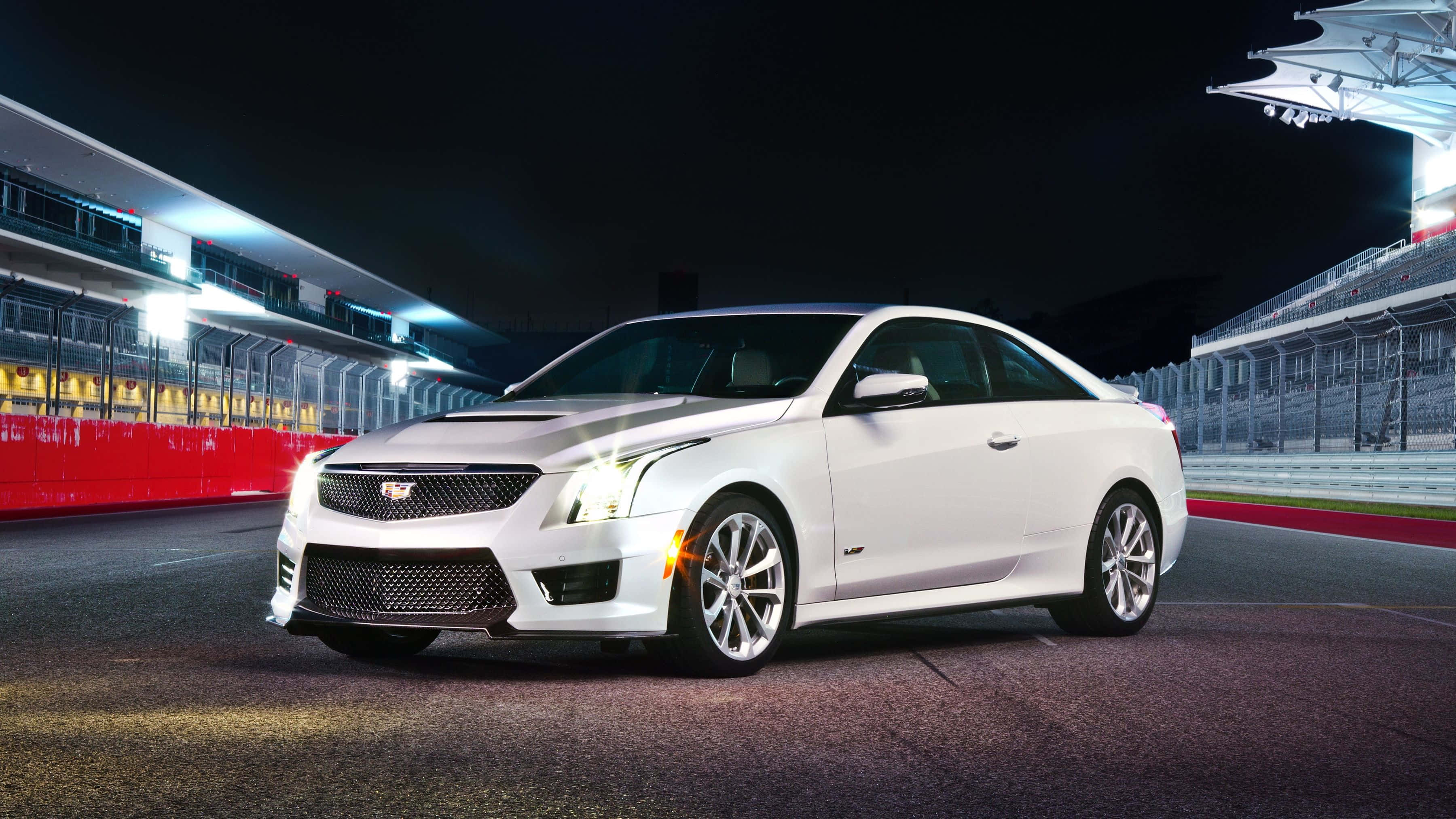 Cadillac Xts 桌布 壁紙 — 一輛時尚的白色凱迪拉克轎跑車在夜間賽車場的賽道燈光下閃閃發光，設有看台和紅色護欄。