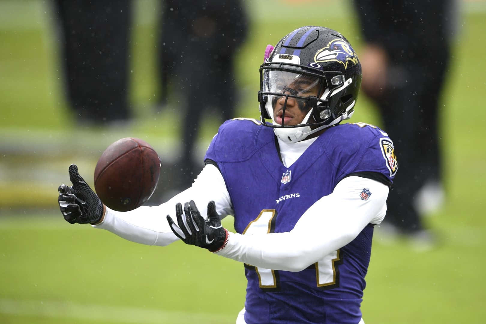  壁紙 — 一名身穿紫色球衣的巴爾的摩烏鴉隊美式足球員在雨中球場上擲球，背景有模糊的人影。