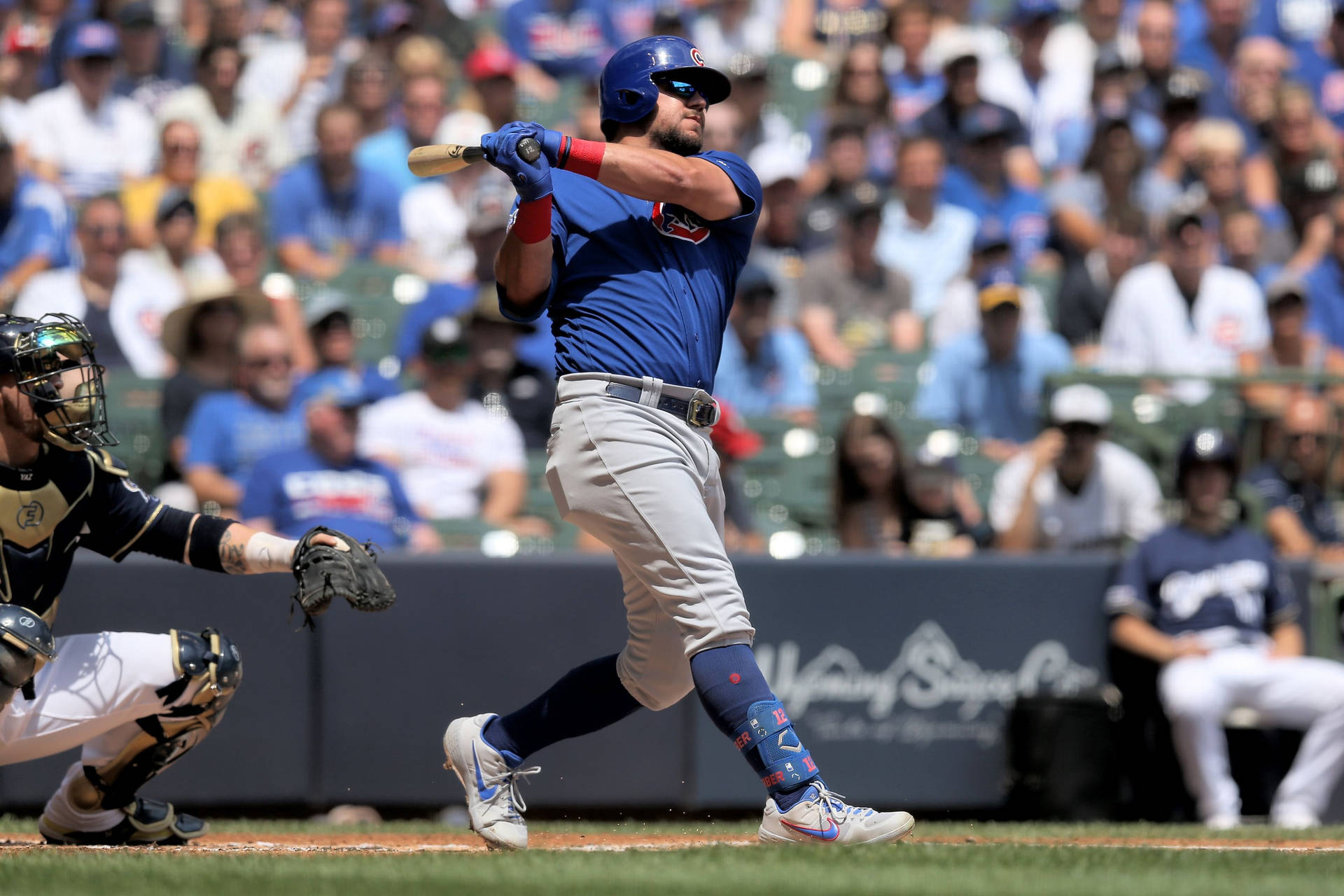 棒球運動員在日間比賽中揮棒，背景有捕手和人群。 — MLB 壁紙