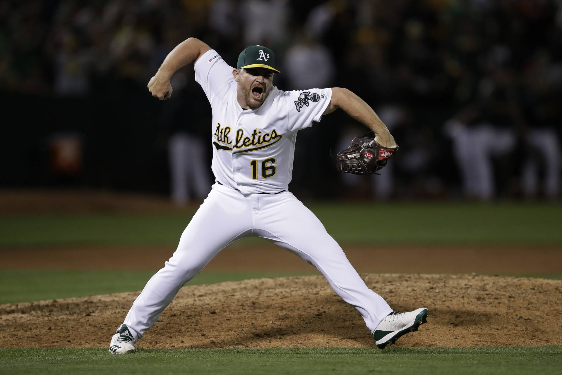 身穿運動家隊球衣的棒球投手在夜間投球。 — MLB 壁紙