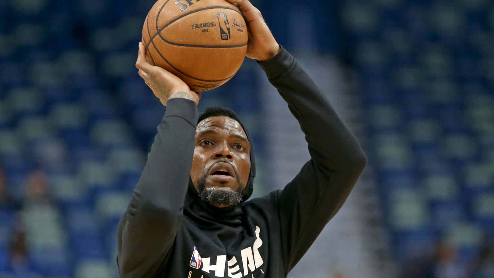  壁紙 — 一名身穿黑色連帽衫的籃球運動員，在模糊的藍色體育場背景下，全神貫注地準備投籃。