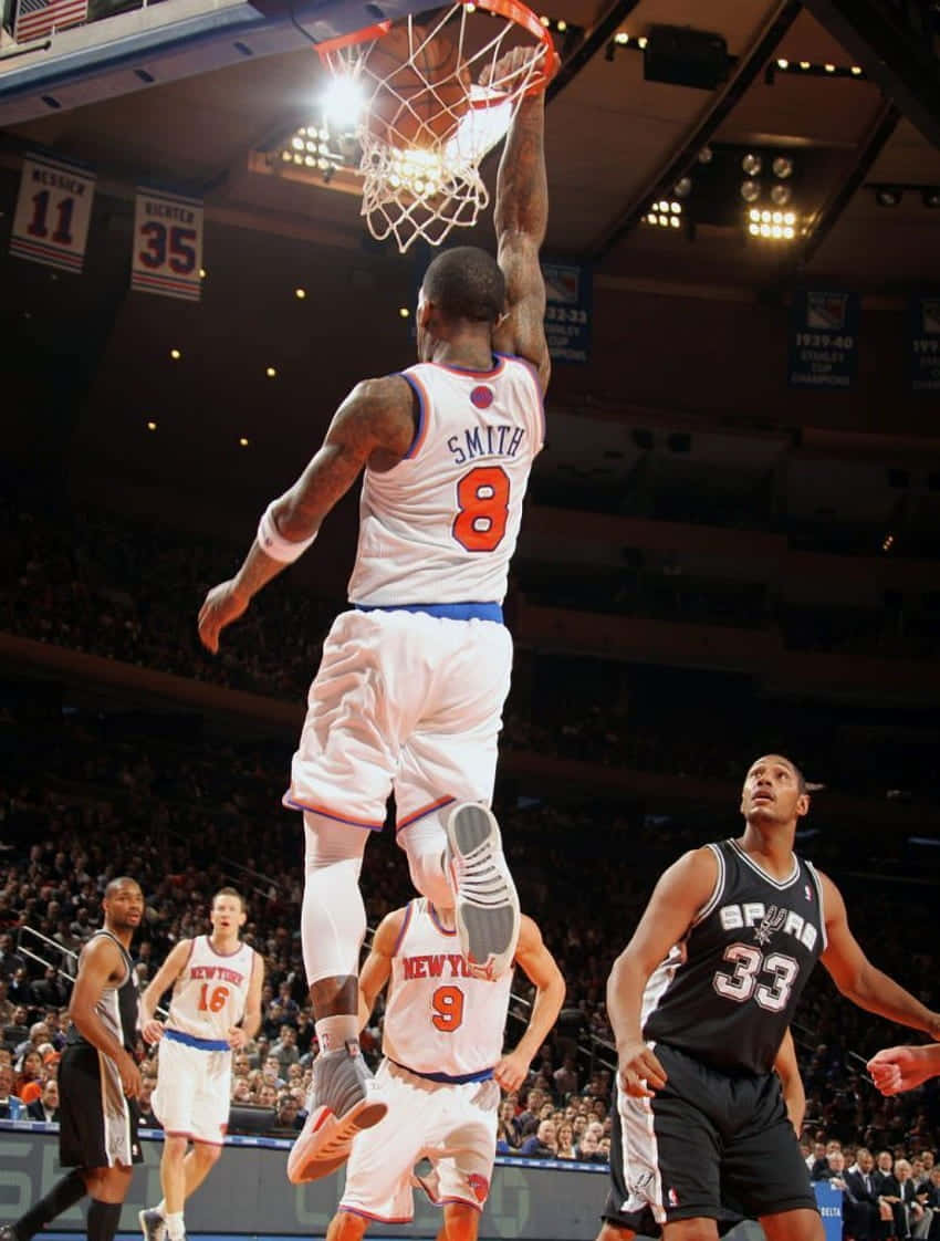 籃球運動員在擠滿觀眾的場館中，於防守球員上方空中灌籃。 — NBA 壁紙