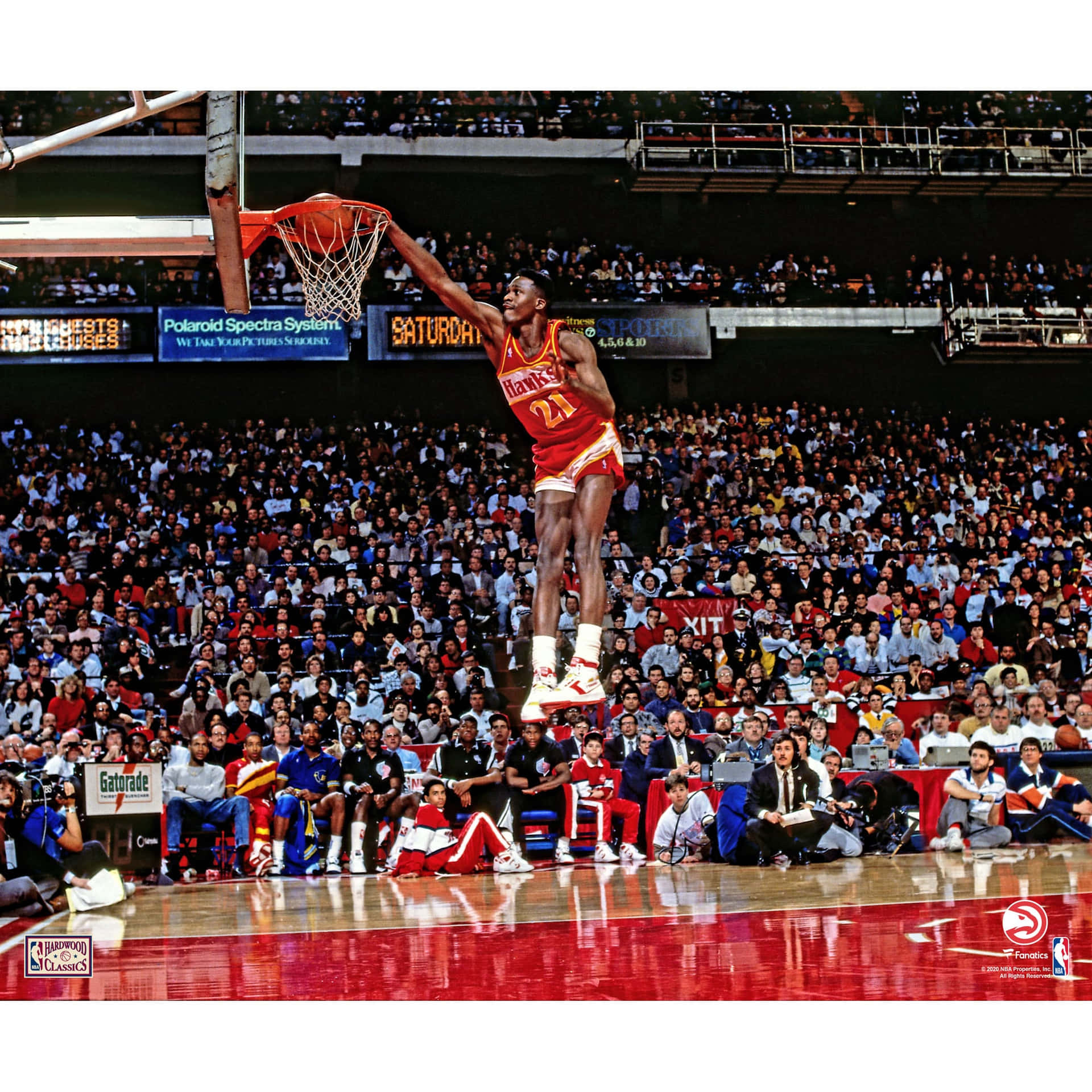 身穿紅色球衣的籃球運動員在擠滿觀眾的體育館上空灌籃。 — NBA 壁紙