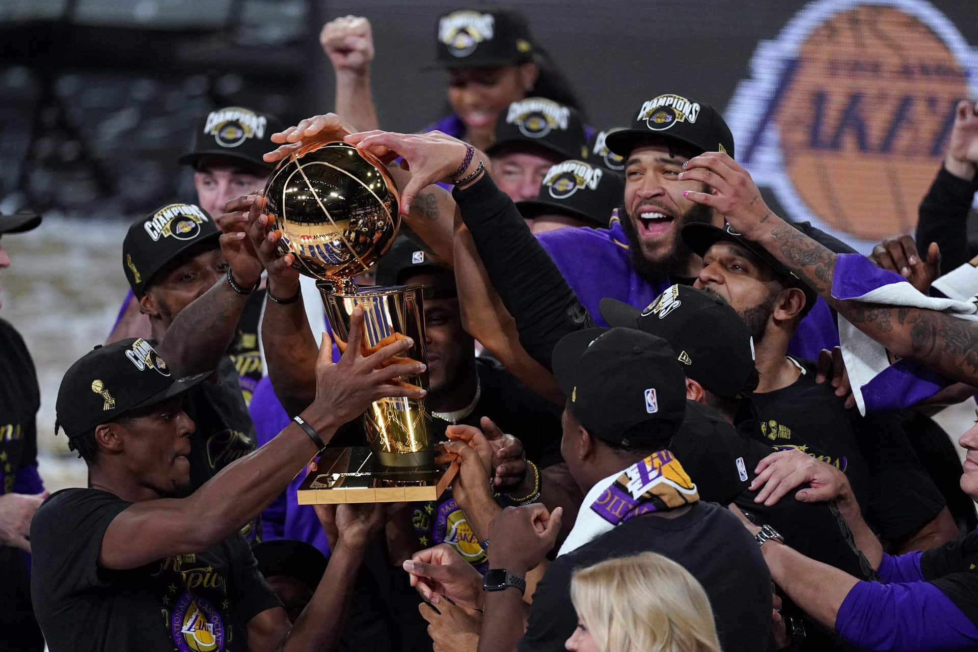  壁紙 — 身穿紫色和金色的籃球運動員一起高舉閃亮的NBA冠軍獎盃，勝利地慶祝。